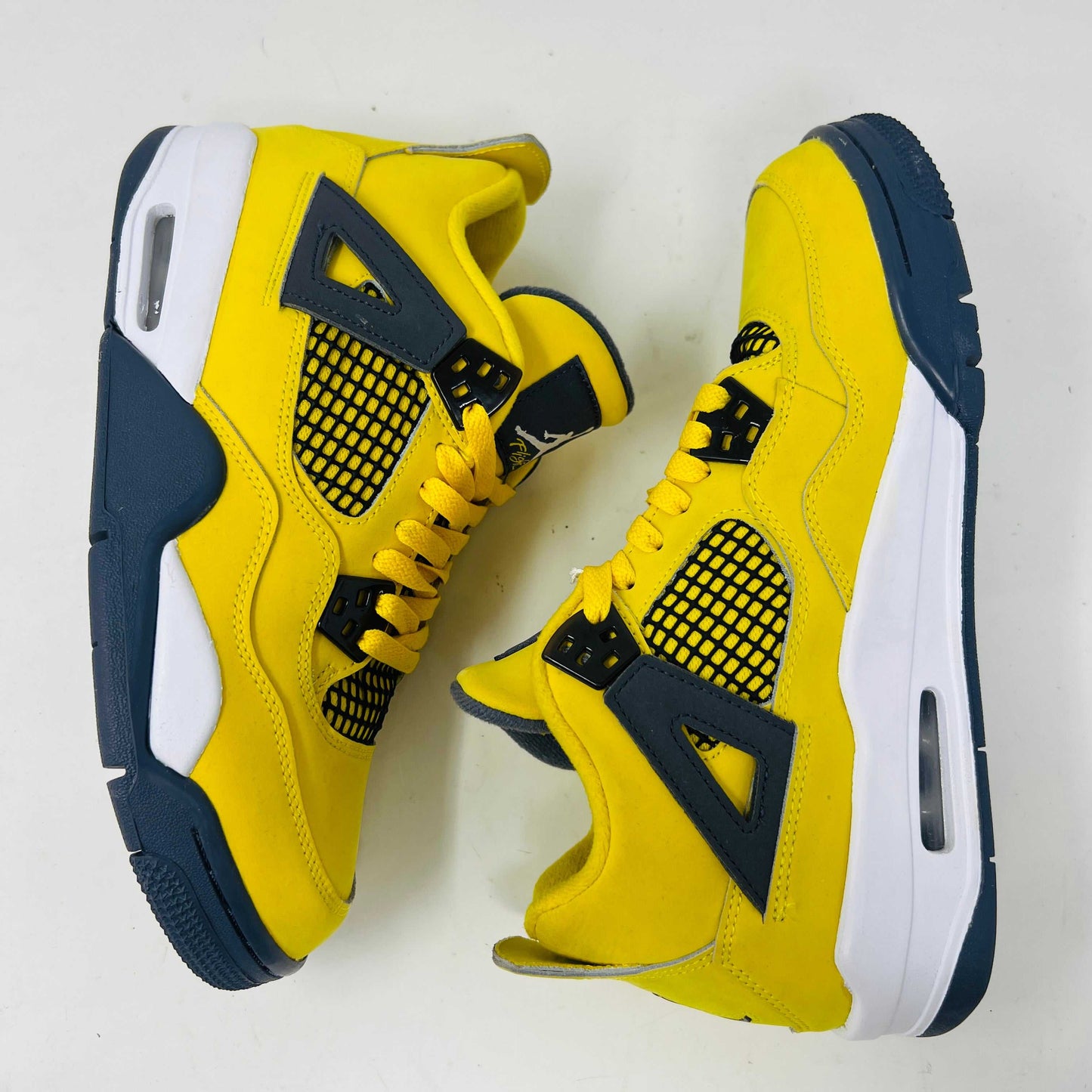 The Jordan 4 Retro Lightning (2021) (GS) sneaker, in bright yellow with black/gray accents and a visible air unit, is displayed on its matching shoebox. Both the box and heel sport the iconic Jumpman logo, with size details confirming authenticity from the Jordan brand.
