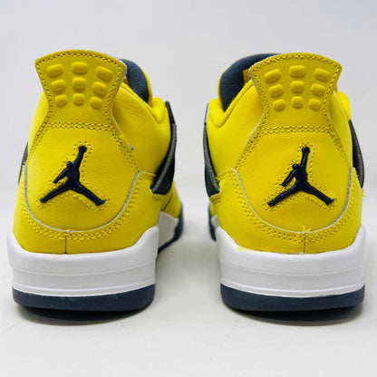 A genuine pair of Jordan 4 Retro Lightning (2021) (GS) in yellow and navy sits on a matching box with a speckled gray base, featuring mesh details, white accents, and the iconic Jumpman logo alongside product info.
