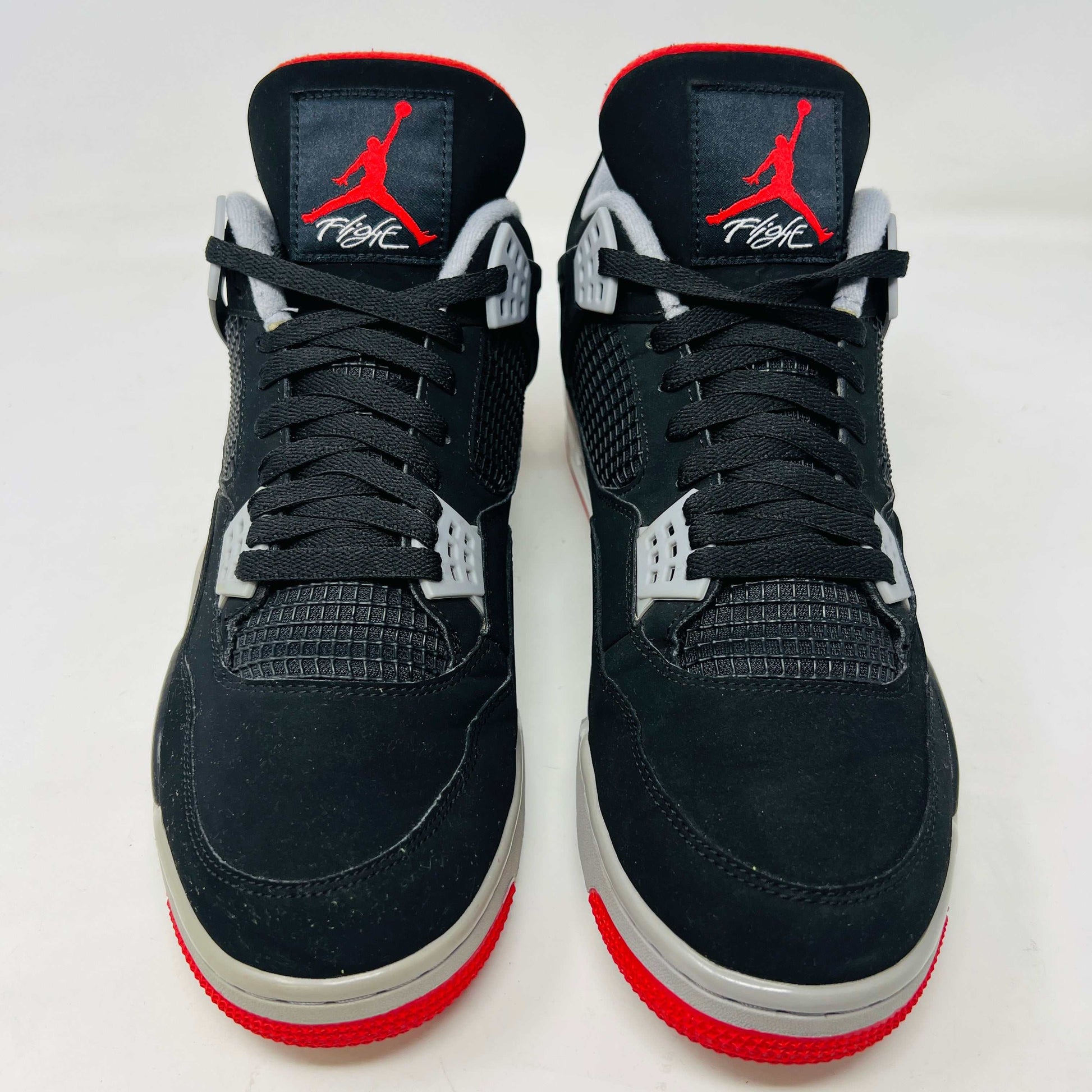 A Jordan 4 Retro Bred (2019) sneaker, featuring black and red colors, clean uppers, slight star loss, mesh paneling, grey accents, and a visible air unit in the heel sits on its box. The box showcases size details and the iconic Jumpman logo to verify its authentic.