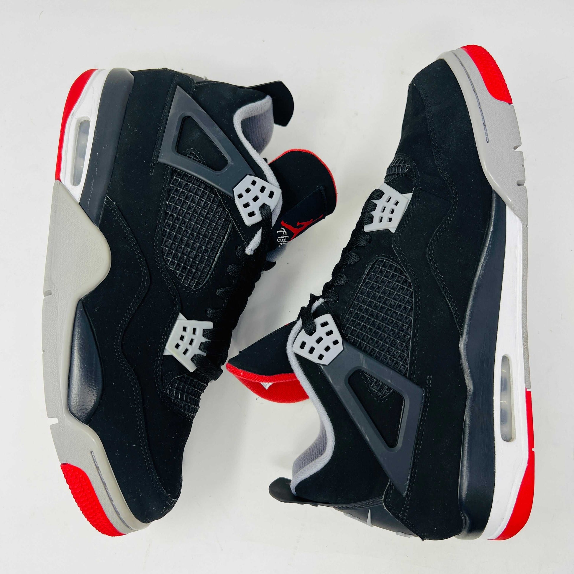 A Jordan 4 Retro Bred (2019) sneaker, featuring black and red colors, clean uppers, slight star loss, mesh paneling, grey accents, and a visible air unit in the heel sits on its box. The box showcases size details and the iconic Jumpman logo to verify its authentic.