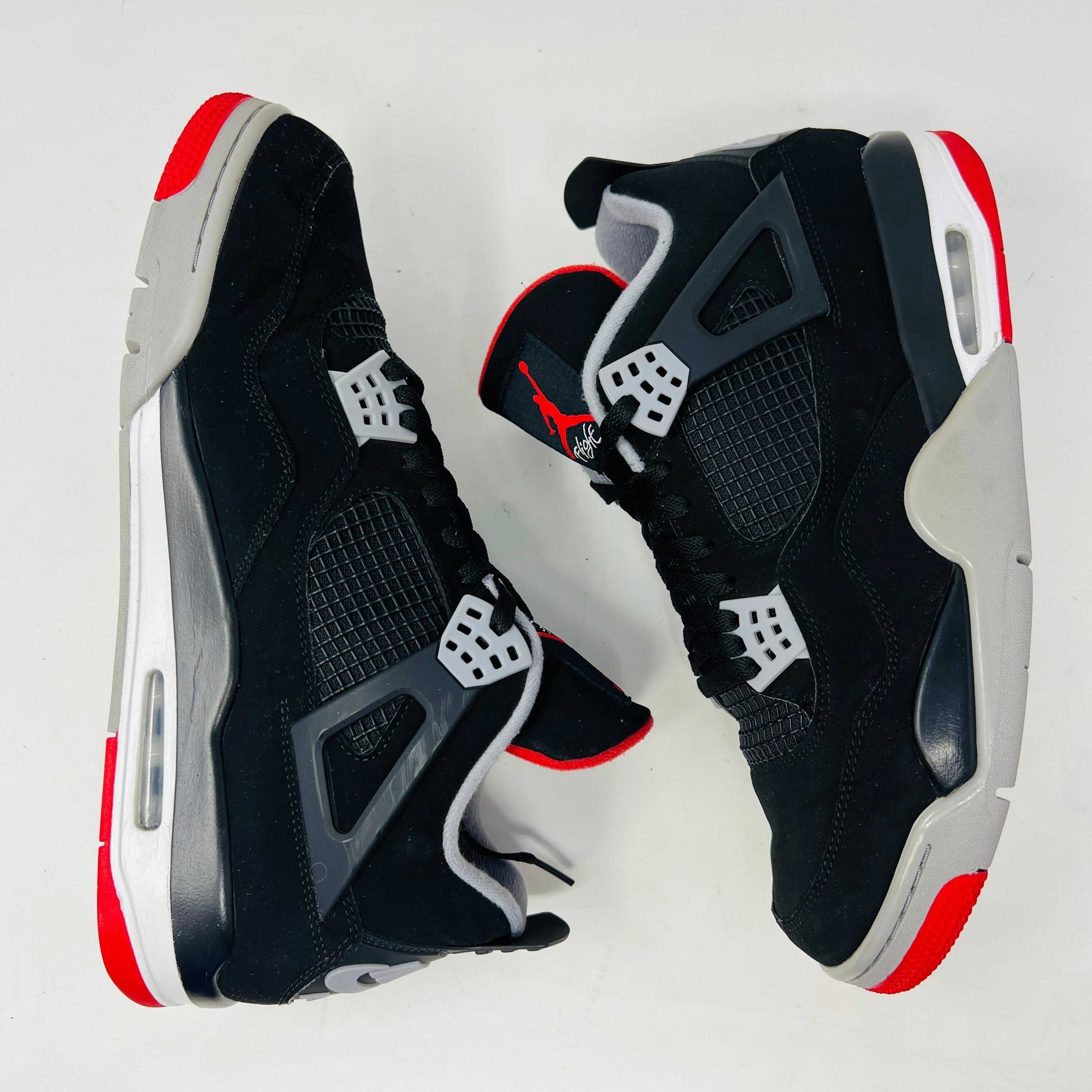 A Jordan 4 Retro Bred (2019) sneaker, featuring black and red colors, clean uppers, slight star loss, mesh paneling, grey accents, and a visible air unit in the heel sits on its box. The box showcases size details and the iconic Jumpman logo to verify its authentic.