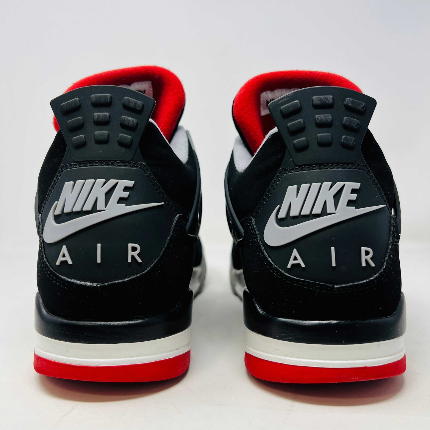 A Jordan 4 Retro Bred (2019) sneaker, featuring black and red colors, clean uppers, slight star loss, mesh paneling, grey accents, and a visible air unit in the heel sits on its box. The box showcases size details and the iconic Jumpman logo to verify its authentic.