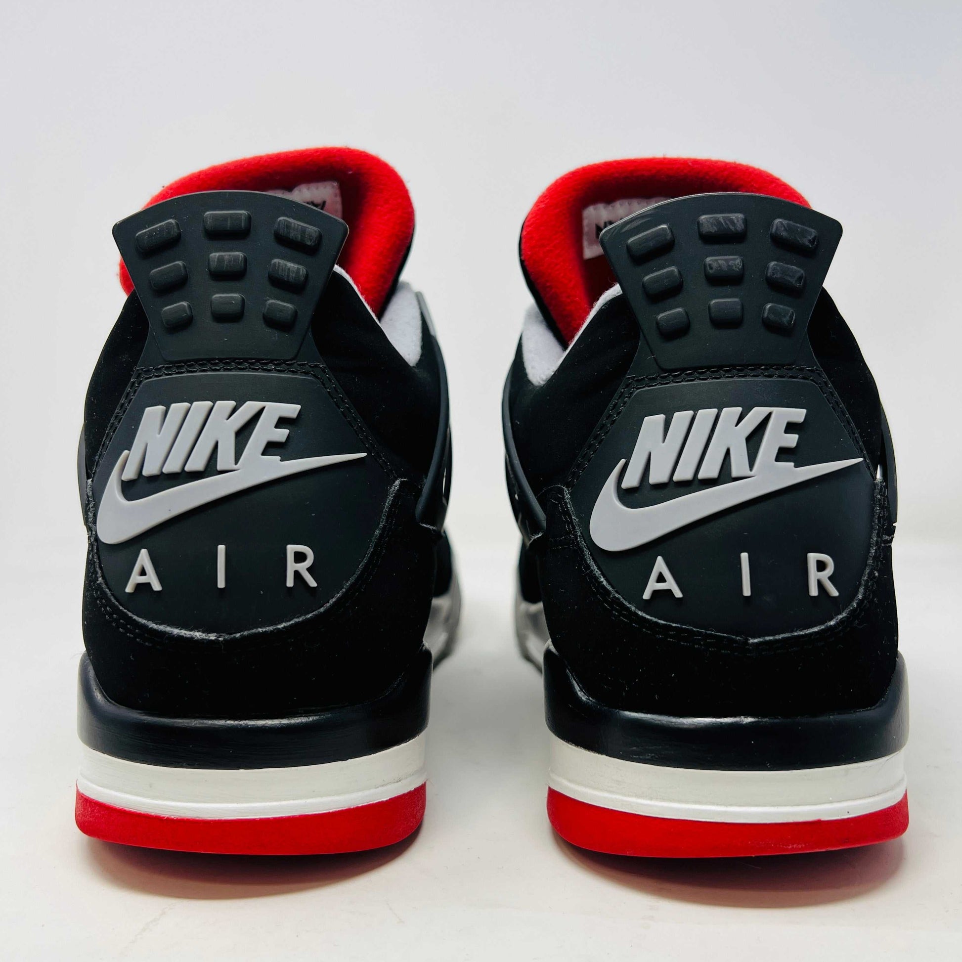 A Jordan 4 Retro Bred (2019) sneaker, featuring black and red colors, clean uppers, slight star loss, mesh paneling, grey accents, and a visible air unit in the heel sits on its box. The box showcases size details and the iconic Jumpman logo to verify its authentic.