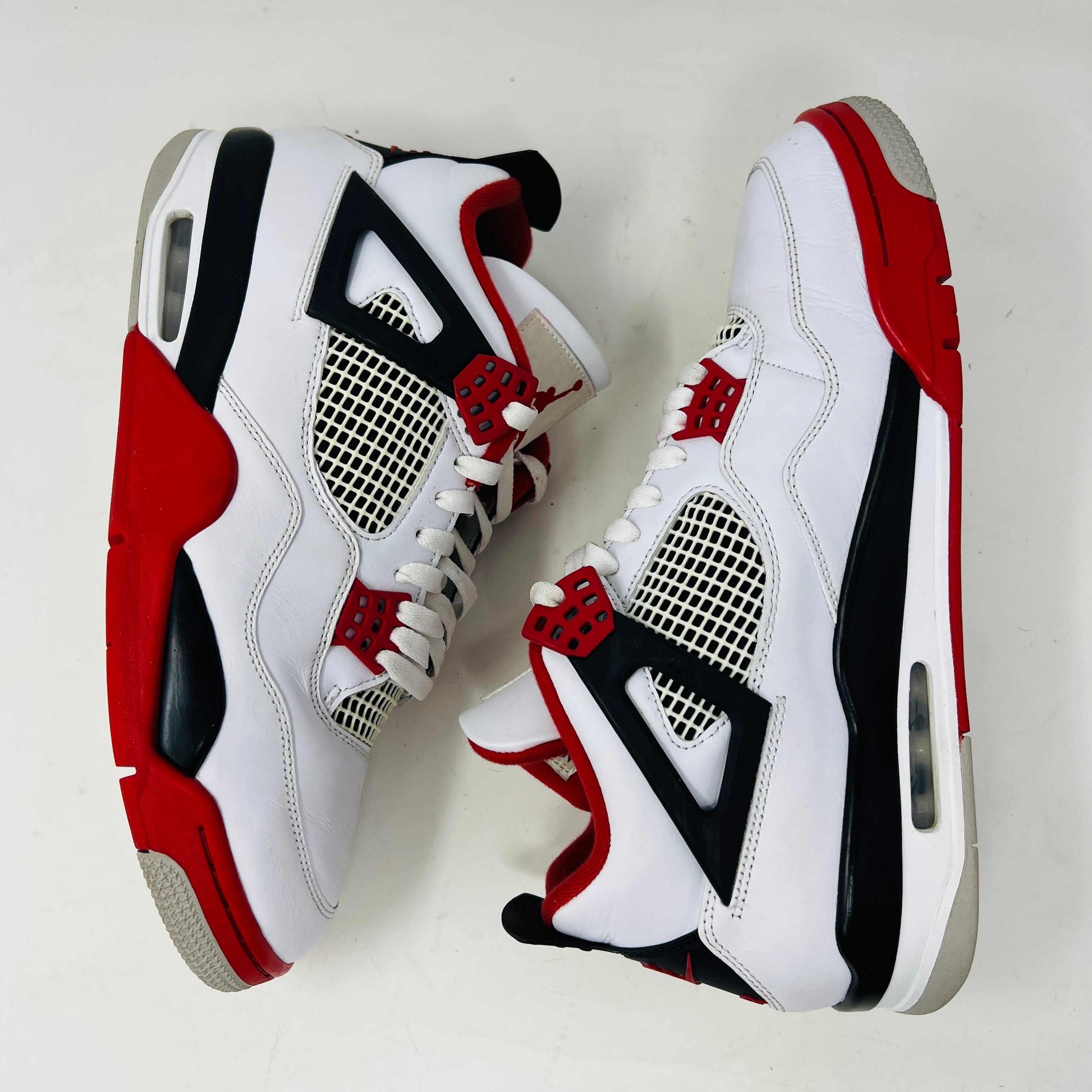 The Jordan 4 Retro Fire Red (2020) sneaker features a white leather upper with red accents, black netting, and a visible Air unit. It rests atop a matching Nike Air branded shoebox, with branding also on the shoe heel.