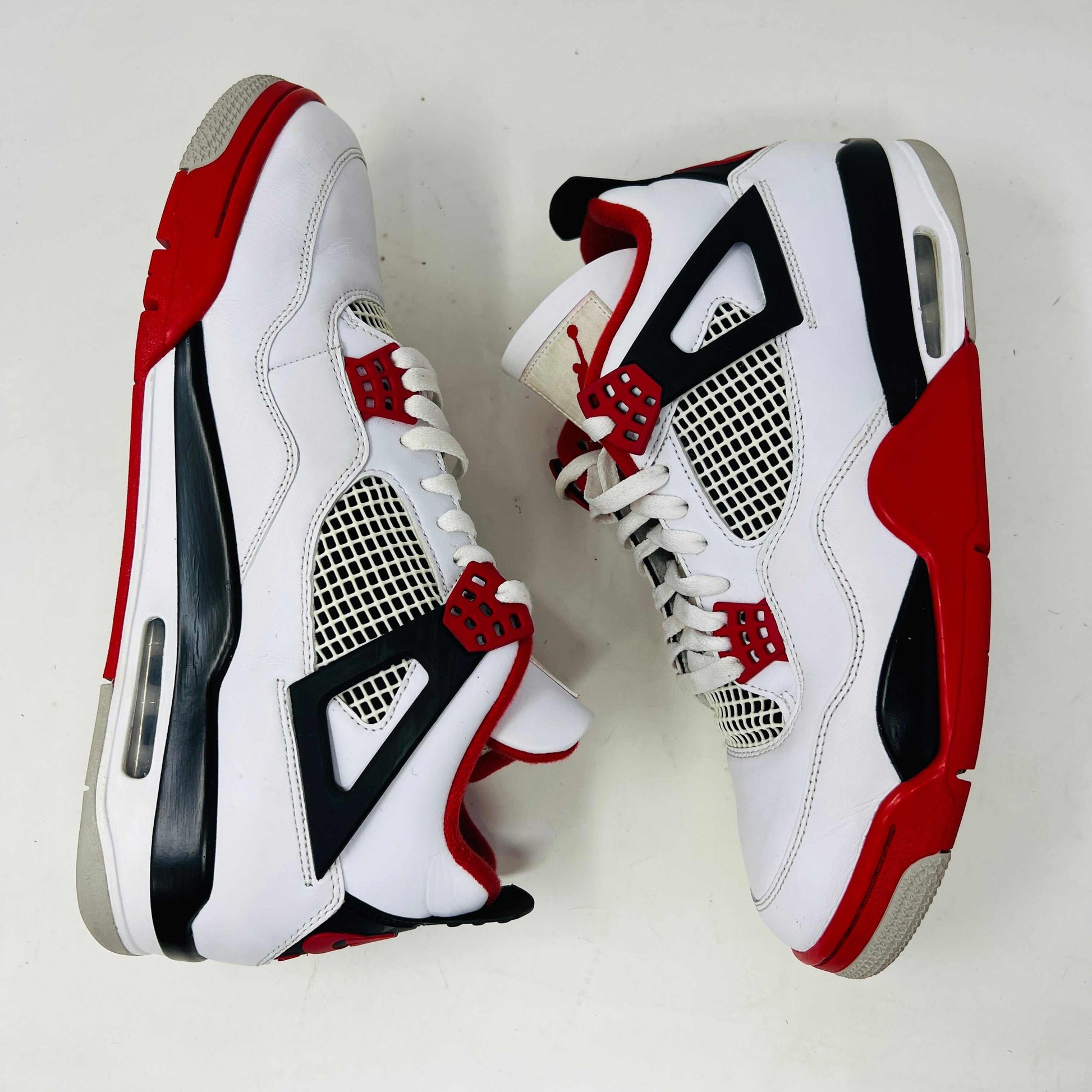 The Jordan 4 Retro Fire Red (2020) sneaker features a white leather upper with red accents, black netting, and a visible Air unit. It rests atop a matching Nike Air branded shoebox, with branding also on the shoe heel.