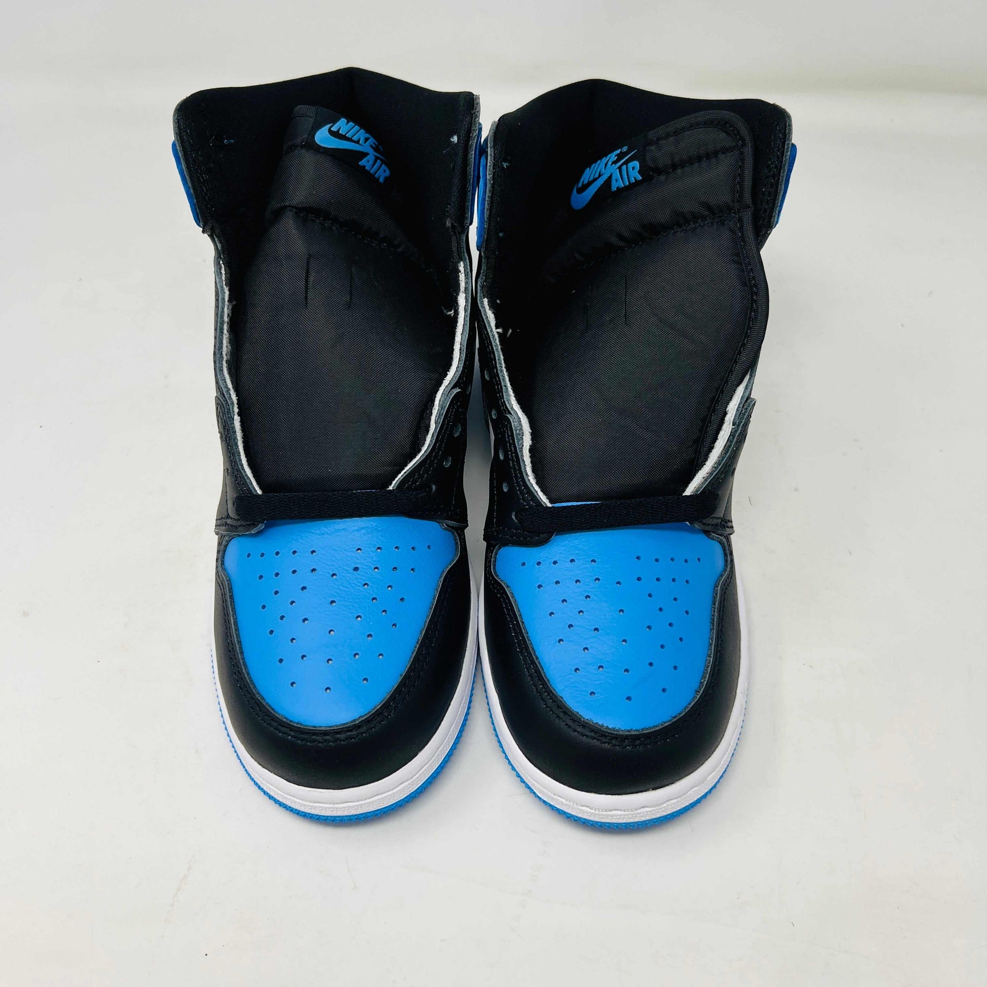 A pair of 100% authentic Jordan 1 Retro High OG UNC Toe (GS) sneakers in black, white, and blue sits on a matching blue box. The shoes feature the iconic black Nike swoosh logo on the side.