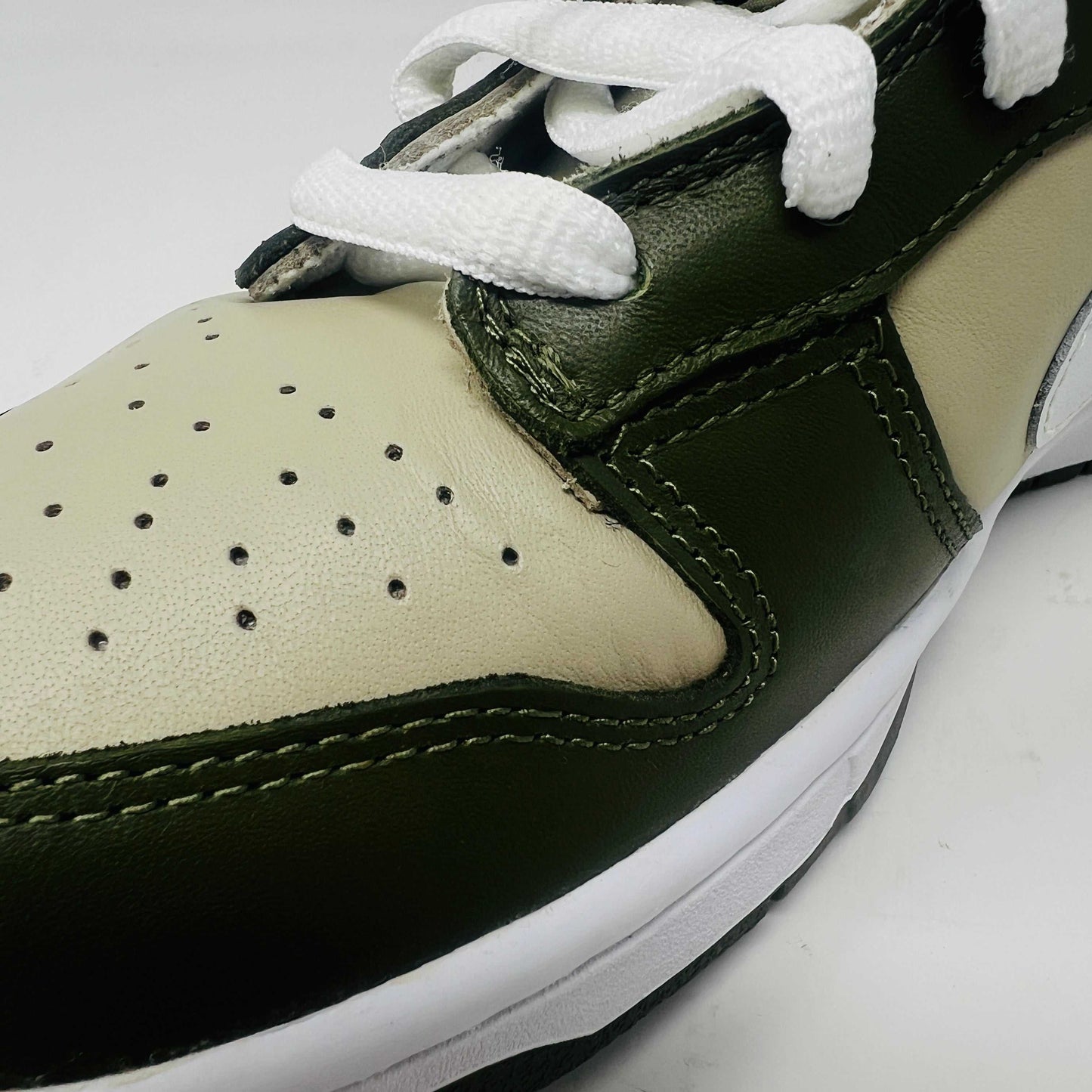 A Nike Dunk Low Light Stone shoe in green and beige with brand new white laces is displayed atop an orange Nike box. Extra white laces are in front, ensuring this 100% authentic pair from the Nike Dunk collection is ready to step out in style.