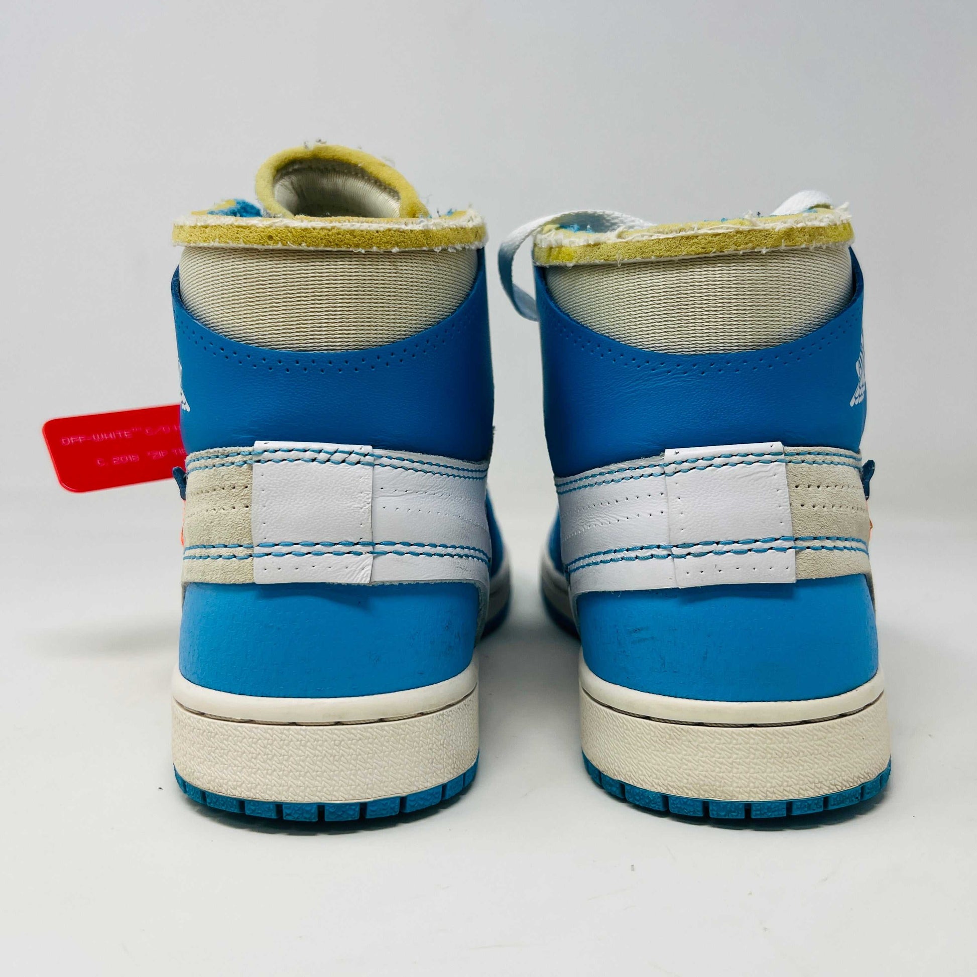 The Jordan 1 Retro High Off-White University Blue, 100% authentic, features clean blue and white uppers with AIR on the sole, orange and blue laces, and a signature red tag. Its styled atop a black and red Nike shoebox.