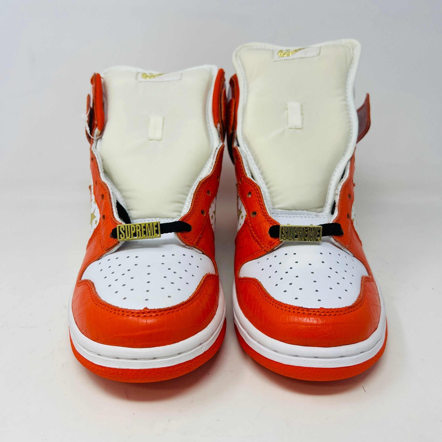 The Nike Dunk High Pro SB Supreme Orange Stars sneaker features an orange and white color scheme with star patterns on the side, a textured finish, and comes with authentic orange and white laces in a separate package.