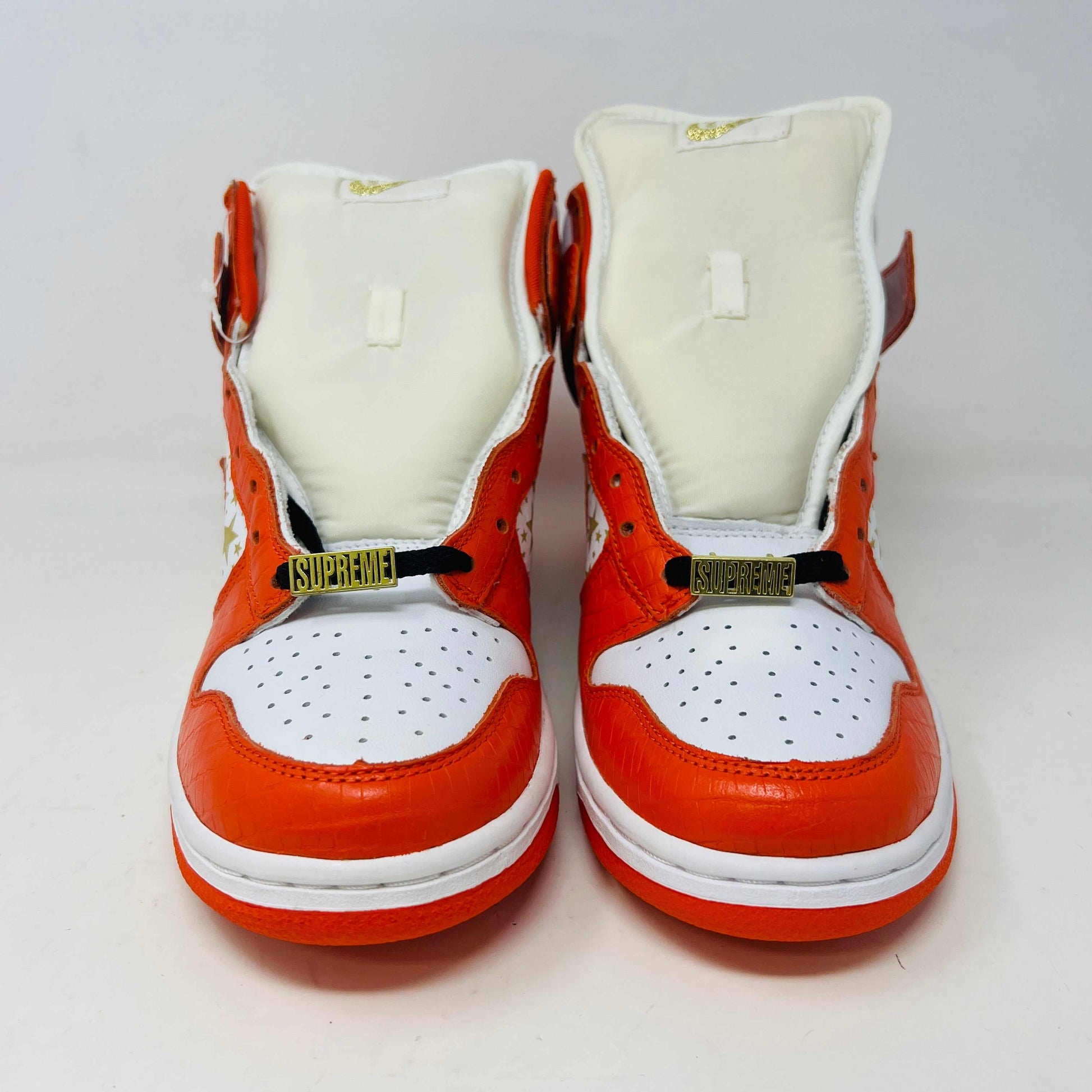 The Nike Dunk High Pro SB Supreme Orange Stars sneaker features an orange and white color scheme with star patterns on the side, a textured finish, and comes with authentic orange and white laces in a separate package.