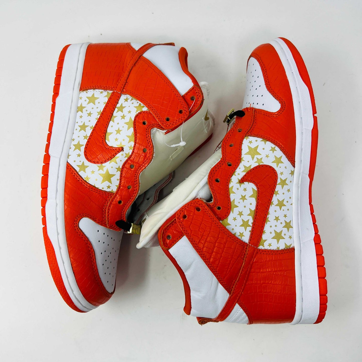 The Nike Dunk High Pro SB Supreme Orange Stars sneaker features an orange and white color scheme with star patterns on the side, a textured finish, and comes with authentic orange and white laces in a separate package.