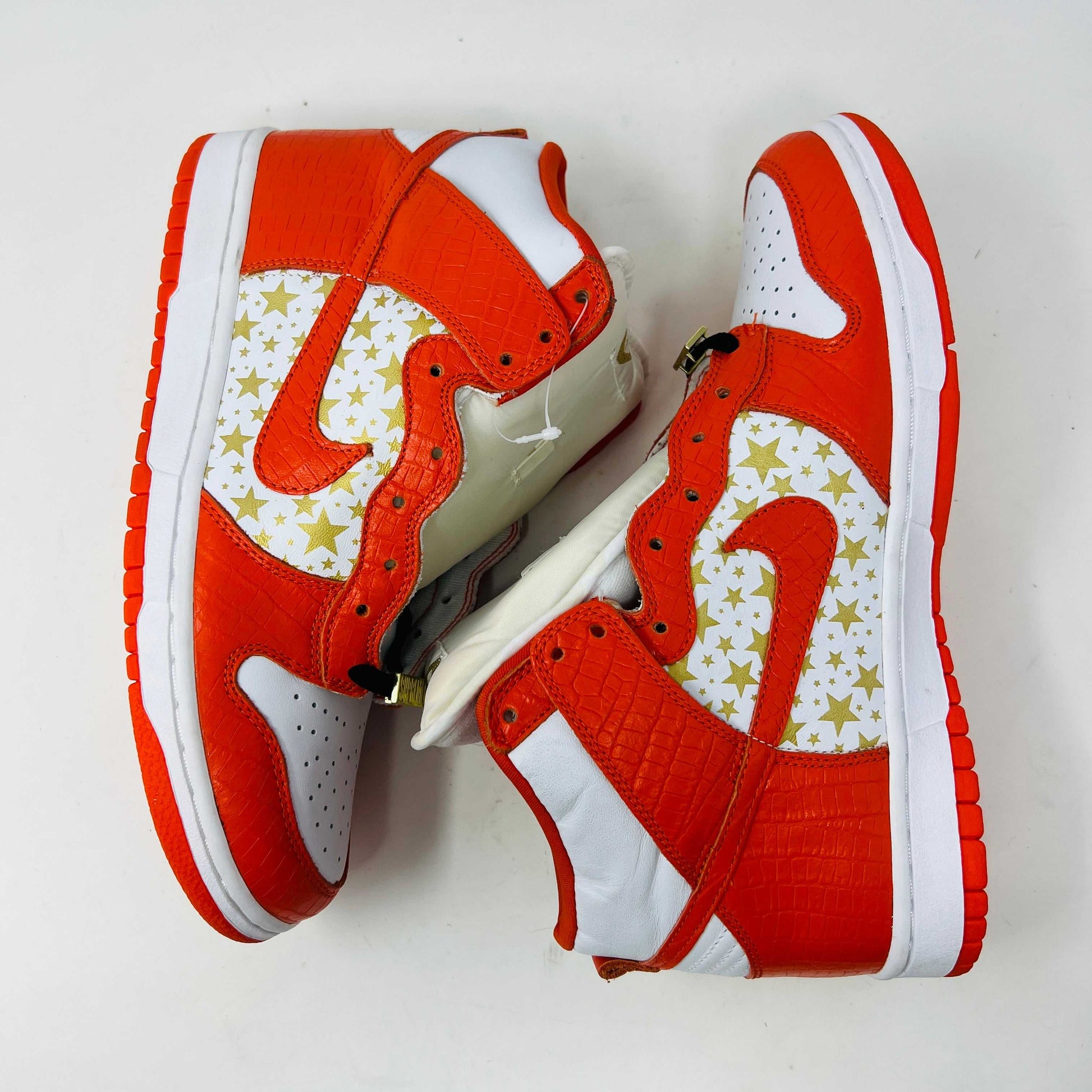 The Nike Dunk High Pro SB Supreme Orange Stars sneaker features an orange and white color scheme with star patterns on the side, a textured finish, and comes with authentic orange and white laces in a separate package.