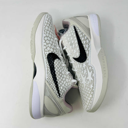 The Nike Kobe 6 Protro Sail All-Star shoes, featuring white textured patterns and black swoosh details with star designs, are elegantly displayed on a sleek black shoebox.