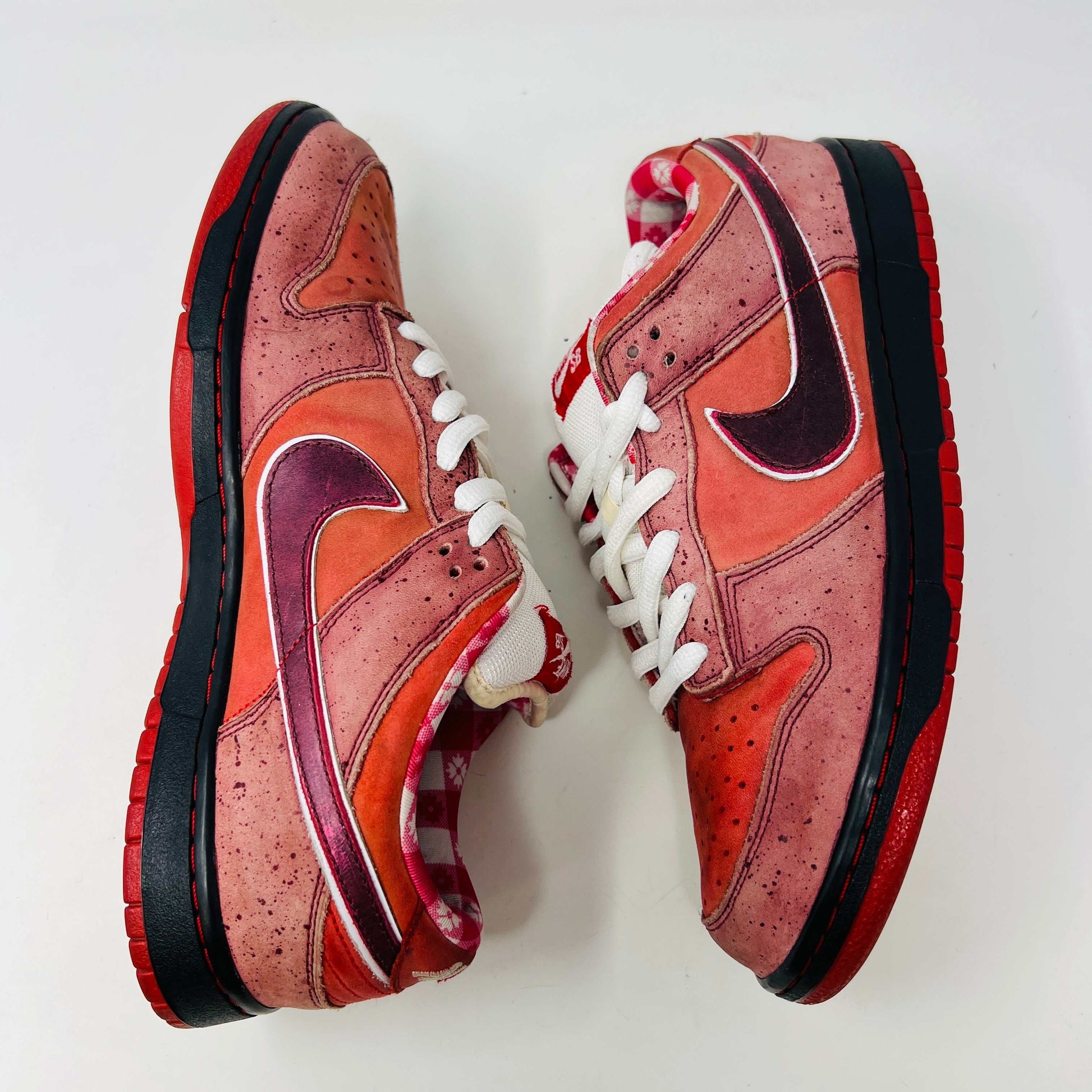 The authentic 2008 Nike SB Dunk Low Concepts Red Lobster features a striking red and pink design with a dark swoosh, complemented by white laces and red accents. It comes in a speckled gray and black replacement box for added flair.