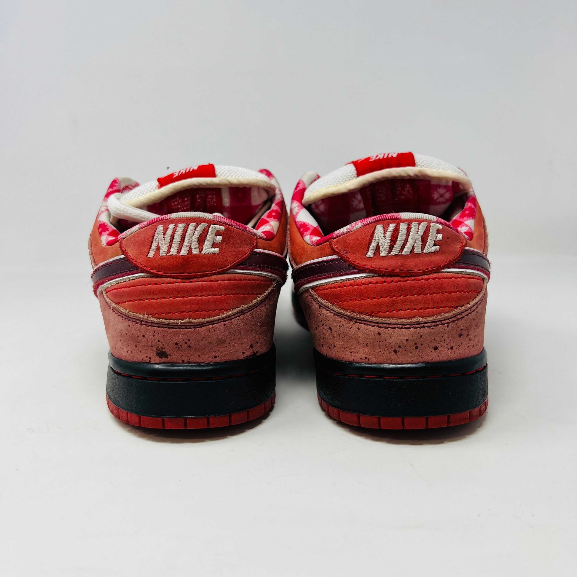 The authentic 2008 Nike SB Dunk Low Concepts Red Lobster features a striking red and pink design with a dark swoosh, complemented by white laces and red accents. It comes in a speckled gray and black replacement box for added flair.