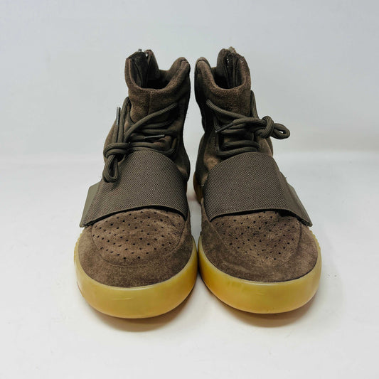 The adidas Yeezy Boost 750 Chocolate sneakers, designed by Yeezy, feature brown suede high-tops with clean uppers and thick ribbed soles. A wide elastic strap and tied laces enhance the sleek look, set against a plain white backdrop. Available on final sale.