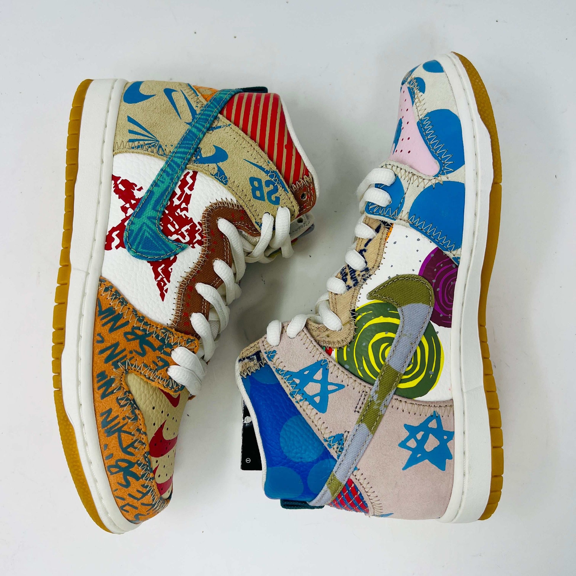The Nike SB Dunk High Thomas Campbell What The Dunk, a colorful high-top sneaker, features a mix of patterns and textures with a blue Nike logo. It is on a teal SB box, BRAND NEW and 100% Authentic. An orange lace lies beside this shoe featuring blue, green, pink, and tan elements.
