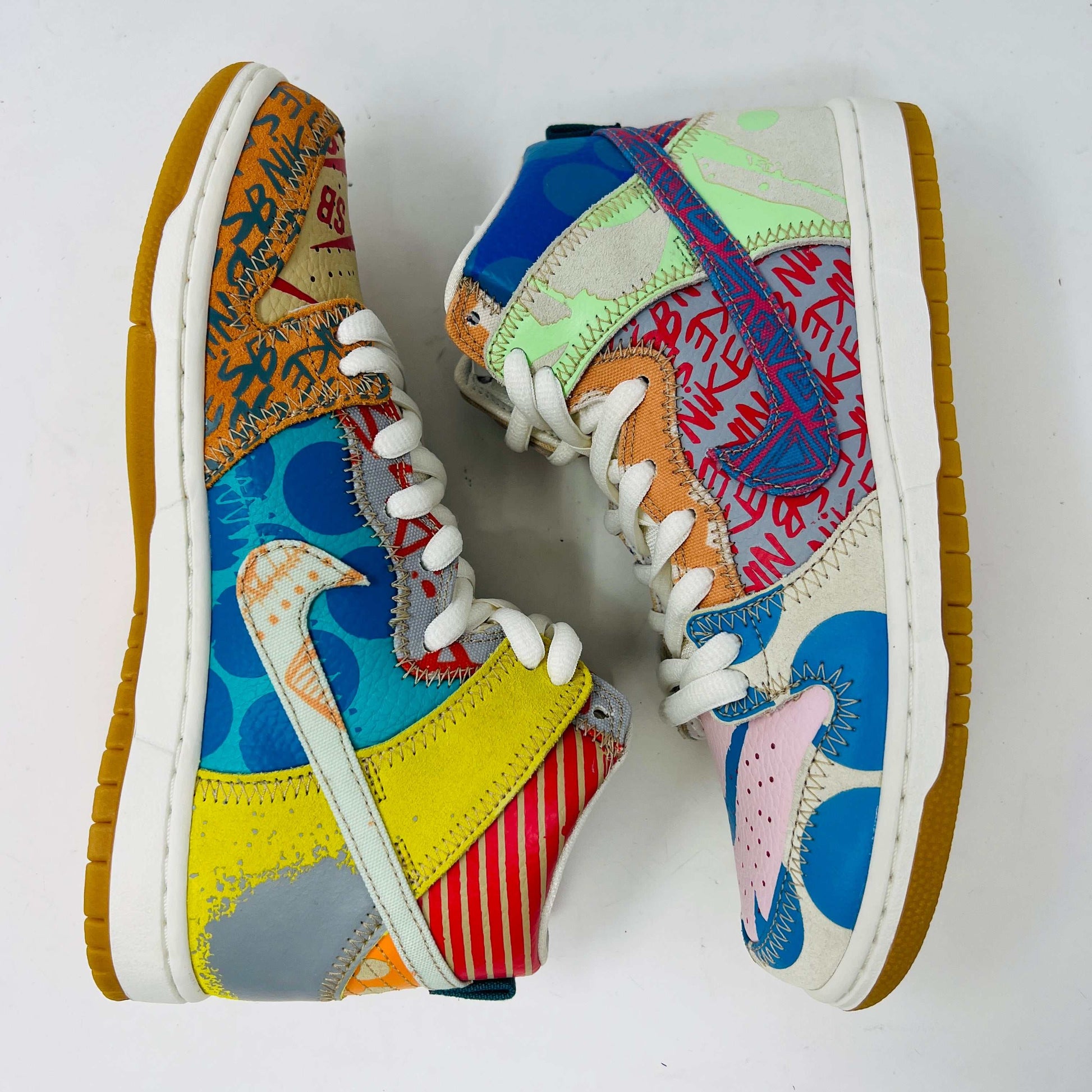 The Nike SB Dunk High Thomas Campbell What The Dunk, a colorful high-top sneaker, features a mix of patterns and textures with a blue Nike logo. It is on a teal SB box, BRAND NEW and 100% Authentic. An orange lace lies beside this shoe featuring blue, green, pink, and tan elements.