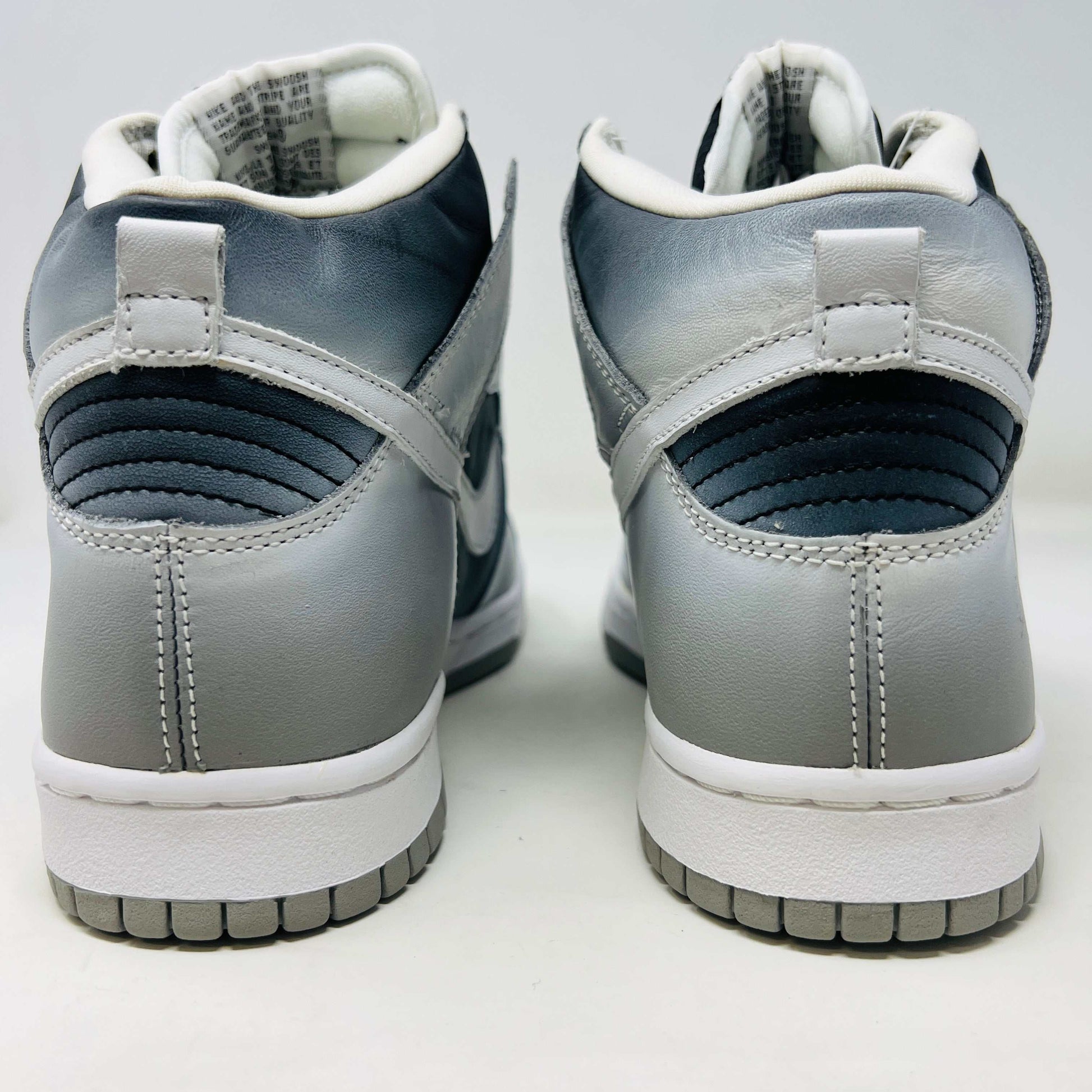 The Nike Dunk High Haze, a brand new and 100% authentic high-top sneaker, showcases a gray and white color scheme with a prominent swoosh and textured sole. It rests on an orange box with the Nike logo, set against a plain white background.