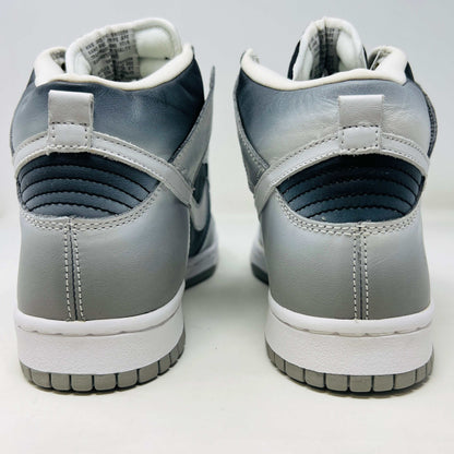 The Nike Dunk High Haze, a brand new and 100% authentic high-top sneaker, showcases a gray and white color scheme with a prominent swoosh and textured sole. It rests on an orange box with the Nike logo, set against a plain white background.