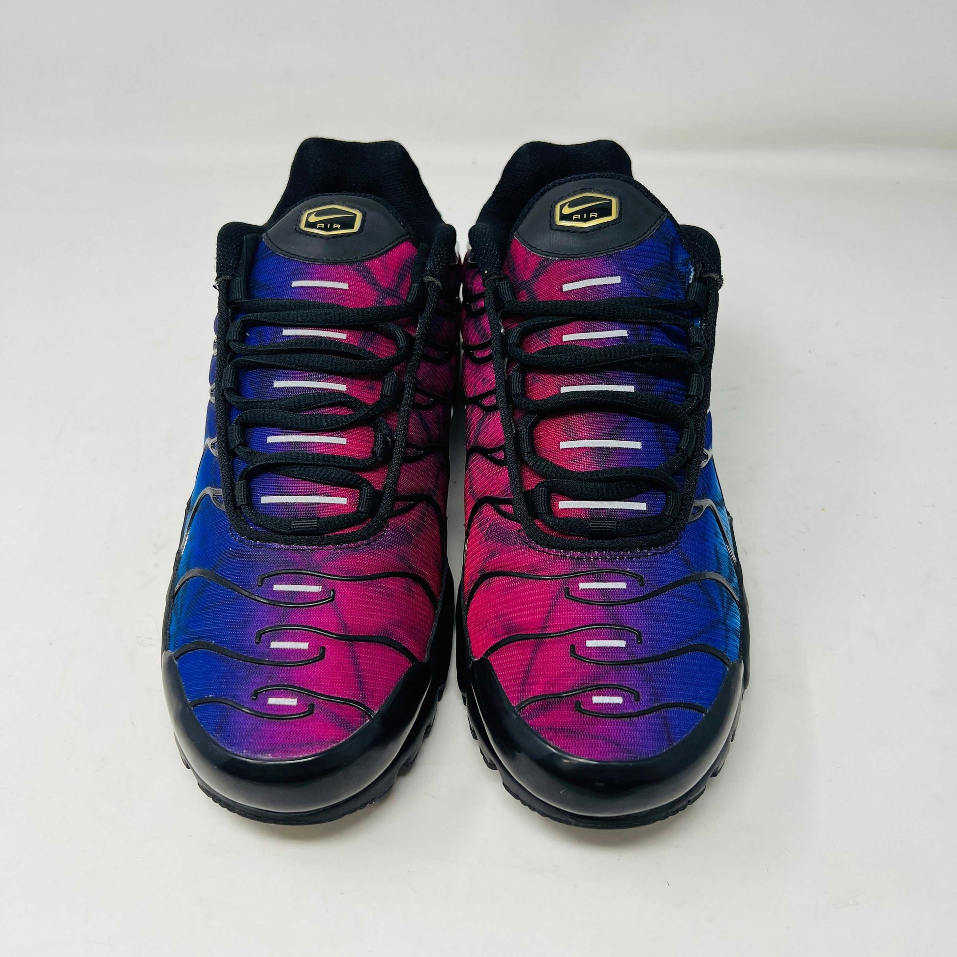 A pair of Nike Air Max Plus 25th Anniversary sneakers, featuring a blue and black wavy color pattern, sits atop a black shoebox. These authentic shoes boast the iconic Nike swoosh and visible air cushioning in the sole.