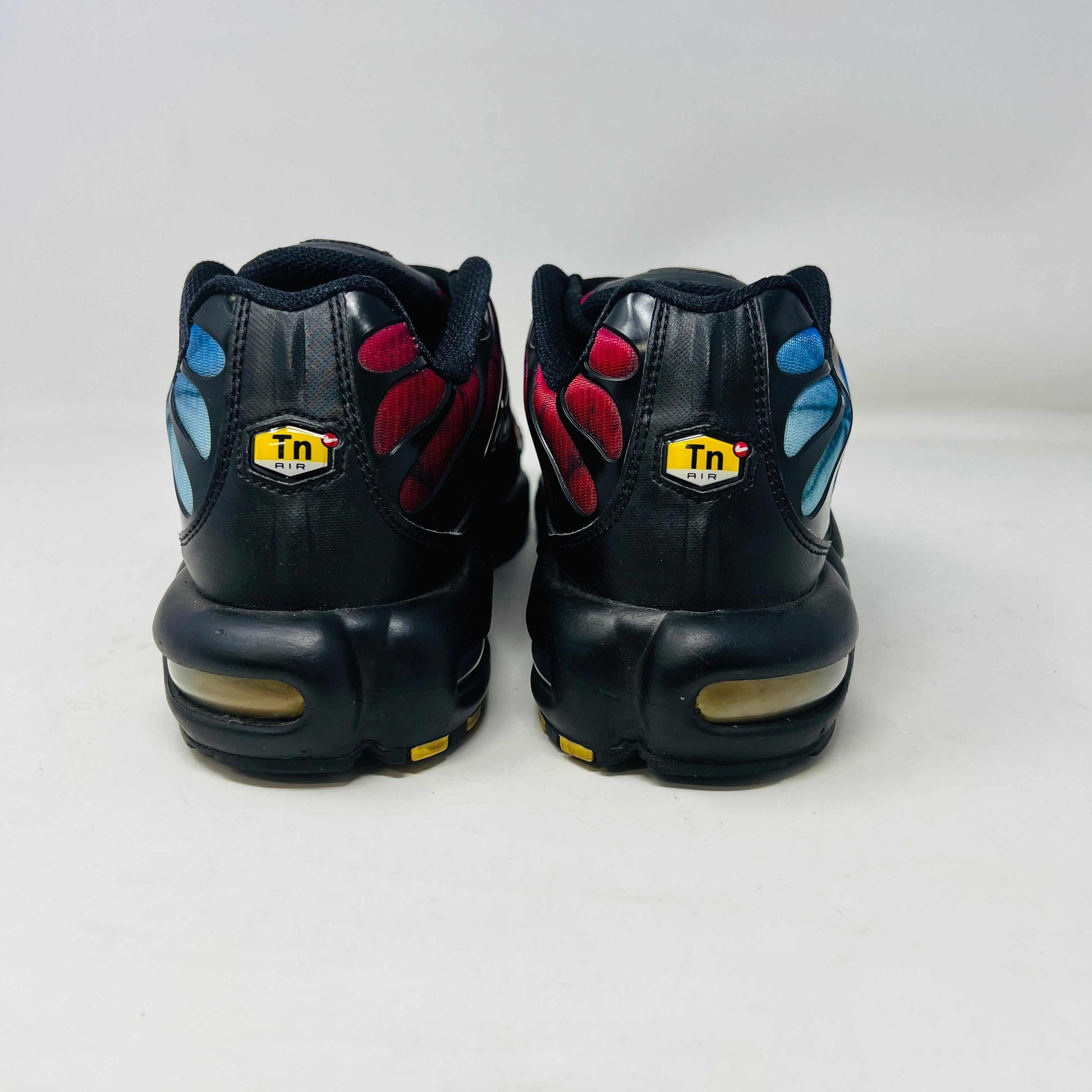 A pair of Nike Air Max Plus 25th Anniversary sneakers, featuring a blue and black wavy color pattern, sits atop a black shoebox. These authentic shoes boast the iconic Nike swoosh and visible air cushioning in the sole.