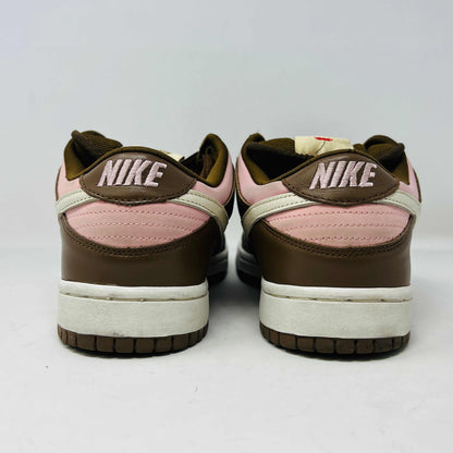 A 2005 Nike SB Dunk Low Stussy Cherry in brown and pink rests on its box, featuring a cream swoosh. The authentic shoe includes extra pink laces in a clear NIKE SB bag. The box label shows size 9.