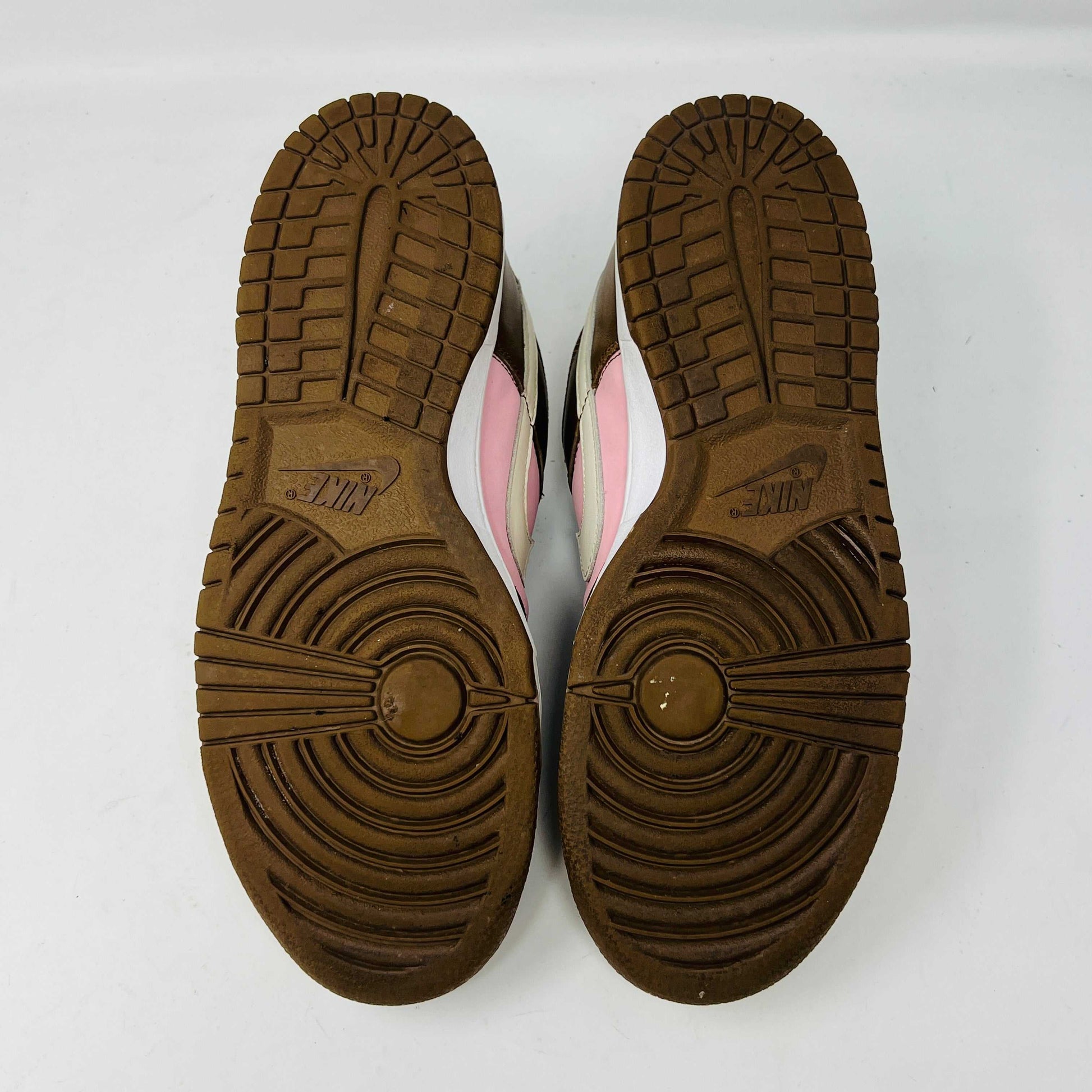 A 2005 Nike SB Dunk Low Stussy Cherry in brown and pink rests on its box, featuring a cream swoosh. The authentic shoe includes extra pink laces in a clear NIKE SB bag. The box label shows size 9.