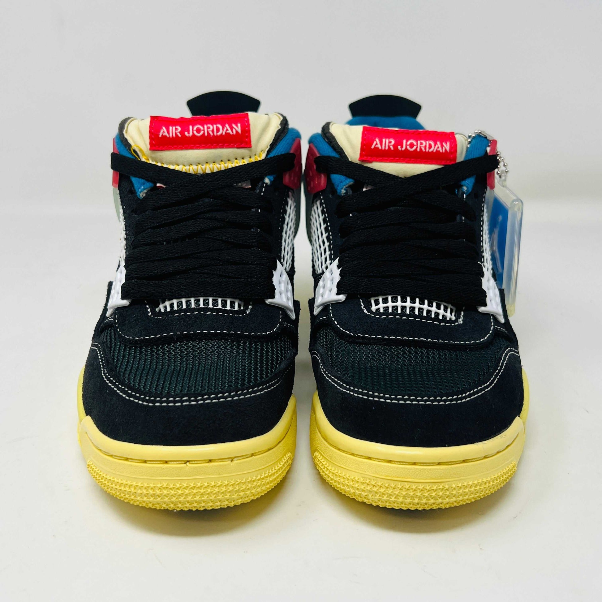 Displayed on their box, the 100% authentic Jordan 4 Retro Union Off Noir sneakers from the Jordan brand showcase clean black uppers, a yellow sole, blue accents, and feature a clear hang tag with a white Jumpman logo. Yellow extra laces are also placed on the box.