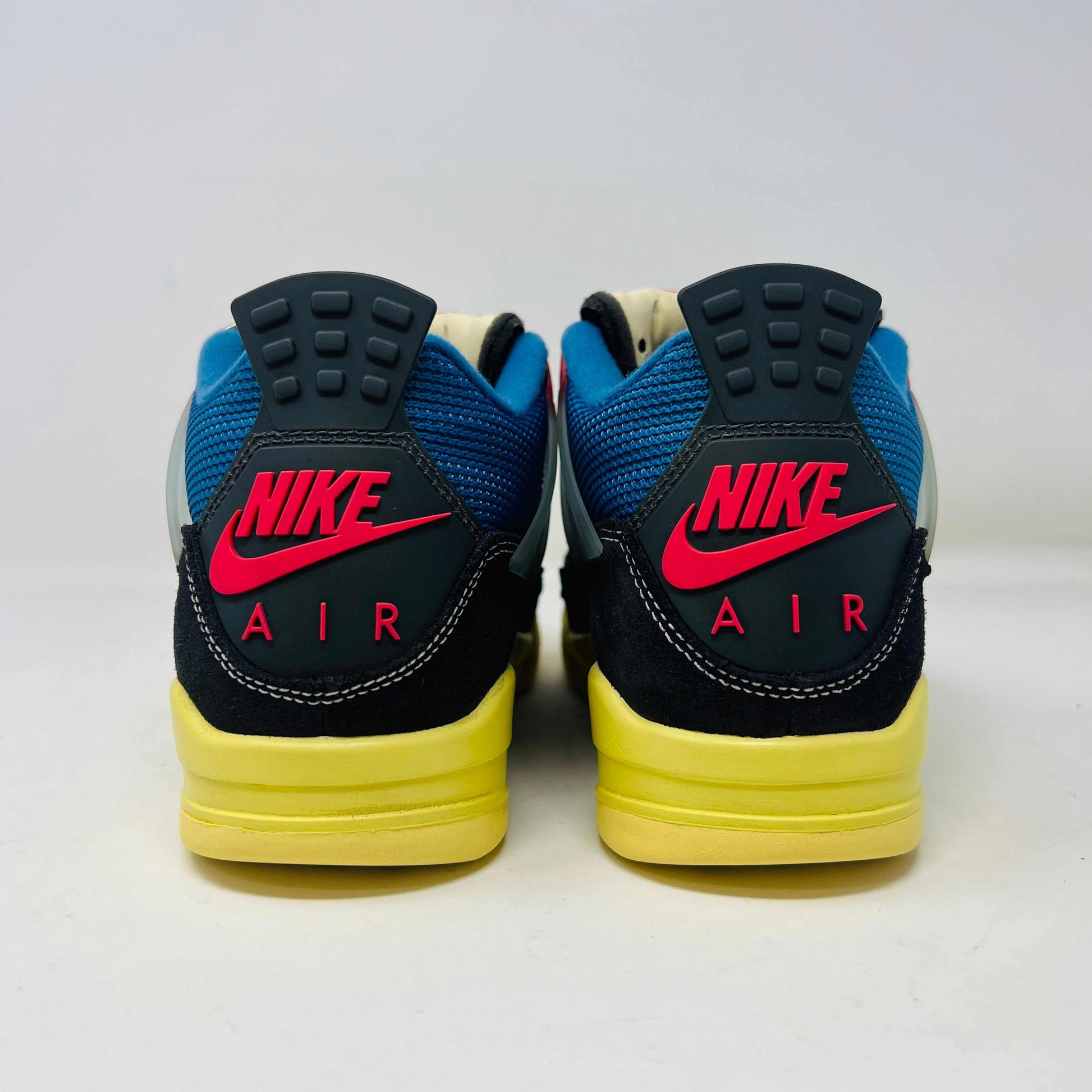 Displayed on their box, the 100% authentic Jordan 4 Retro Union Off Noir sneakers from the Jordan brand showcase clean black uppers, a yellow sole, blue accents, and feature a clear hang tag with a white Jumpman logo. Yellow extra laces are also placed on the box.