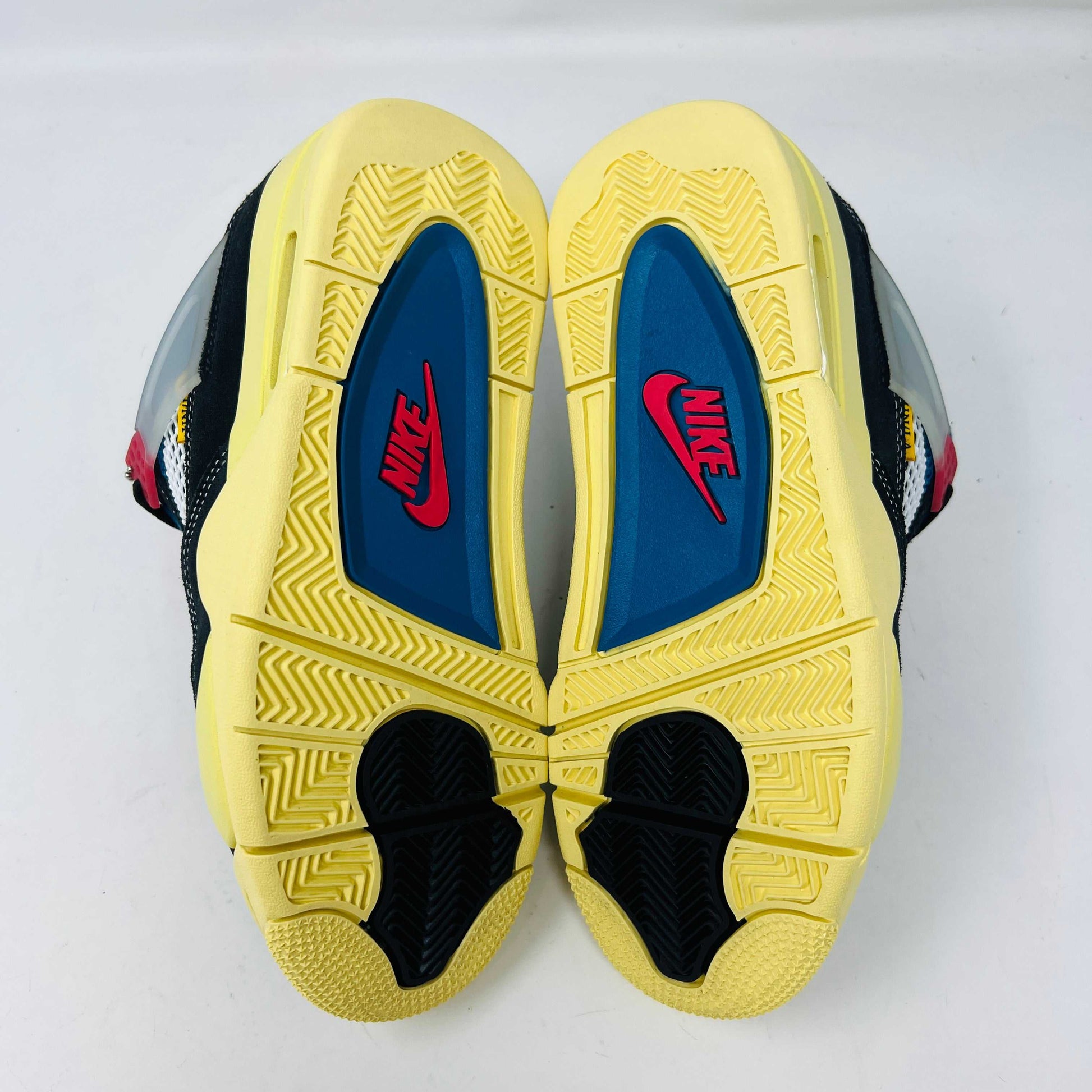 Displayed on their box, the 100% authentic Jordan 4 Retro Union Off Noir sneakers from the Jordan brand showcase clean black uppers, a yellow sole, blue accents, and feature a clear hang tag with a white Jumpman logo. Yellow extra laces are also placed on the box.