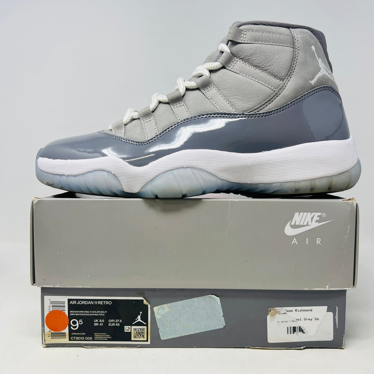 The Jordan 11 Retro Cool Grey (2021) sneaker, featuring clean gray and white uppers with glossy patent leather accents and white laces, is displayed on a gray Nike Air shoebox. The shoe is authentic in size 9.5, with the box in good condition.