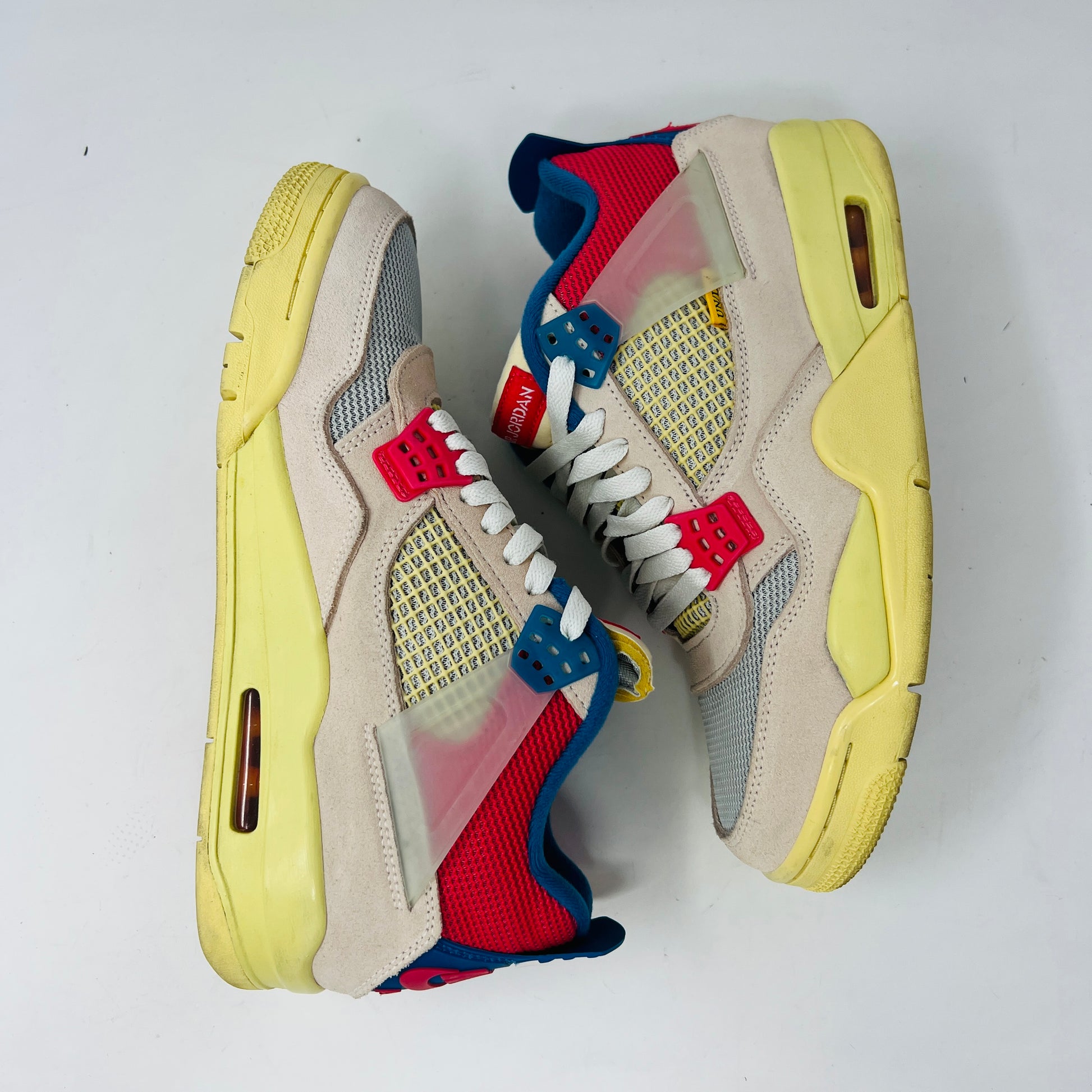 The Jordan 4 Retro Union Guava Ice sneaker from Jordan features a vibrant mix of beige, yellow, blue, and red on its clean uppers. It includes extra yellow laces packaged in a plastic bag alongside the shoe box.
