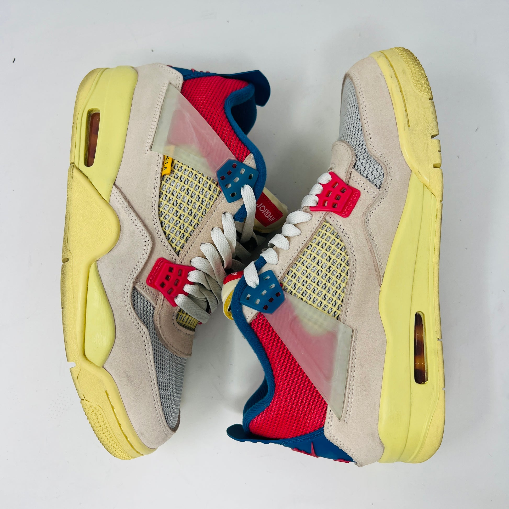 The Jordan 4 Retro Union Guava Ice sneaker from Jordan features a vibrant mix of beige, yellow, blue, and red on its clean uppers. It includes extra yellow laces packaged in a plastic bag alongside the shoe box.