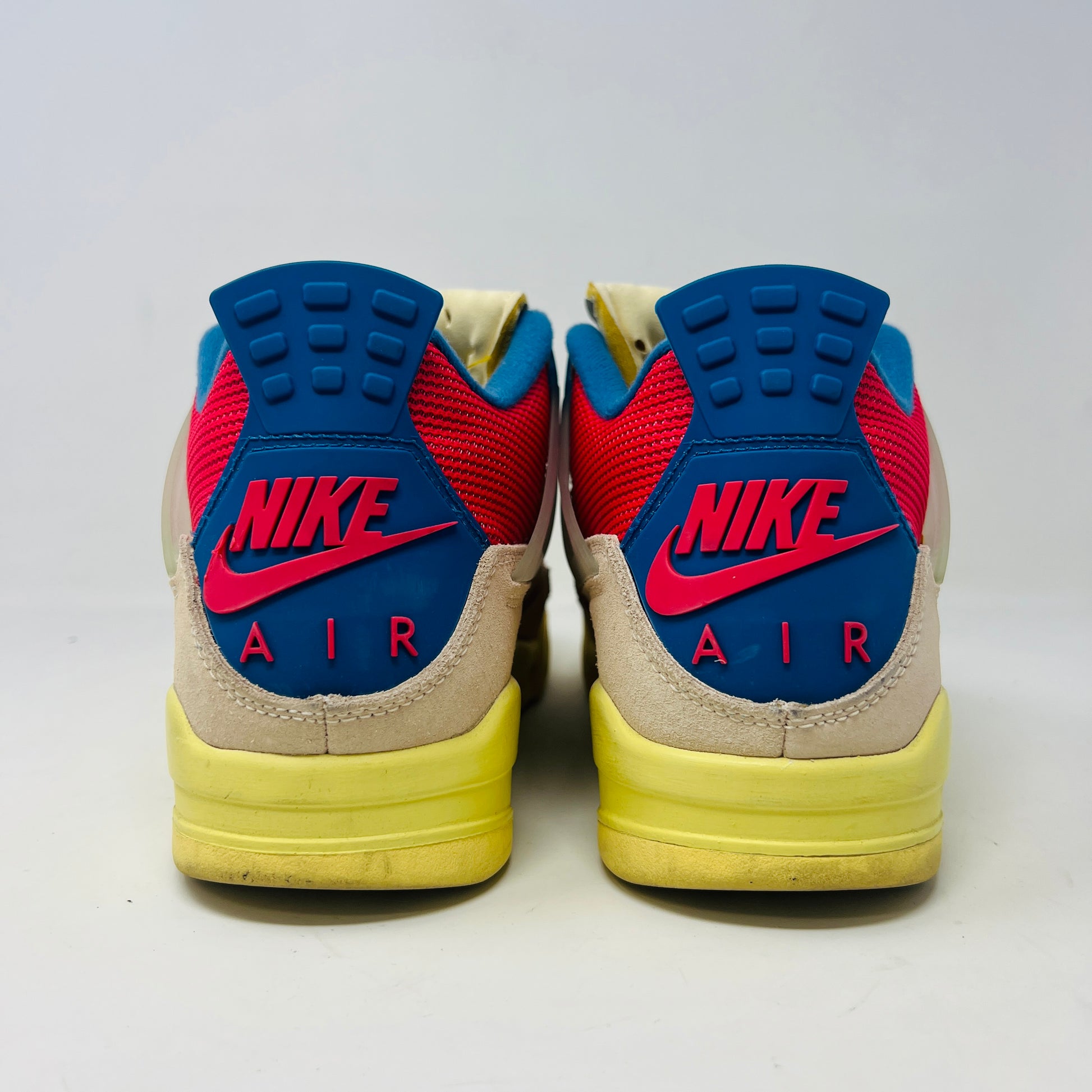 The Jordan 4 Retro Union Guava Ice sneaker from Jordan features a vibrant mix of beige, yellow, blue, and red on its clean uppers. It includes extra yellow laces packaged in a plastic bag alongside the shoe box.