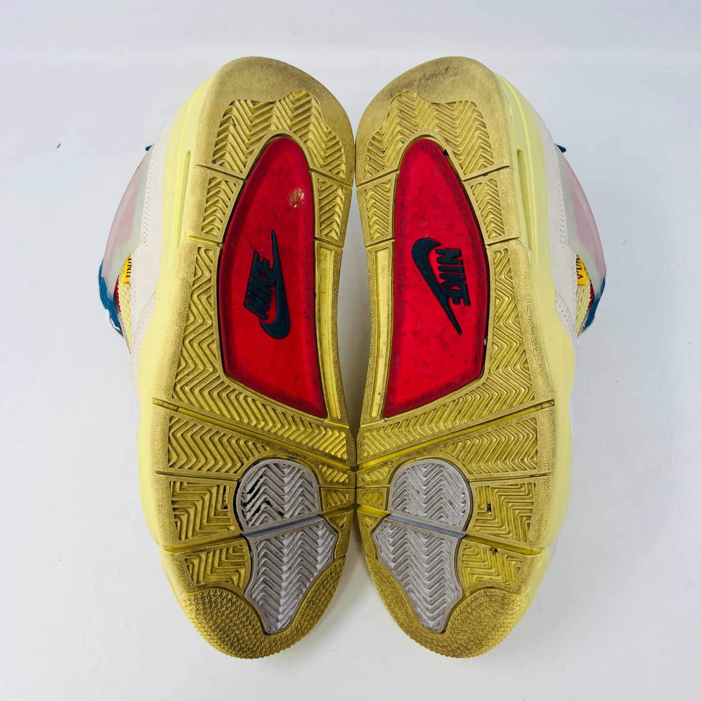The Jordan 4 Retro Union Guava Ice sneaker from Jordan features a vibrant mix of beige, yellow, blue, and red on its clean uppers. It includes extra yellow laces packaged in a plastic bag alongside the shoe box.