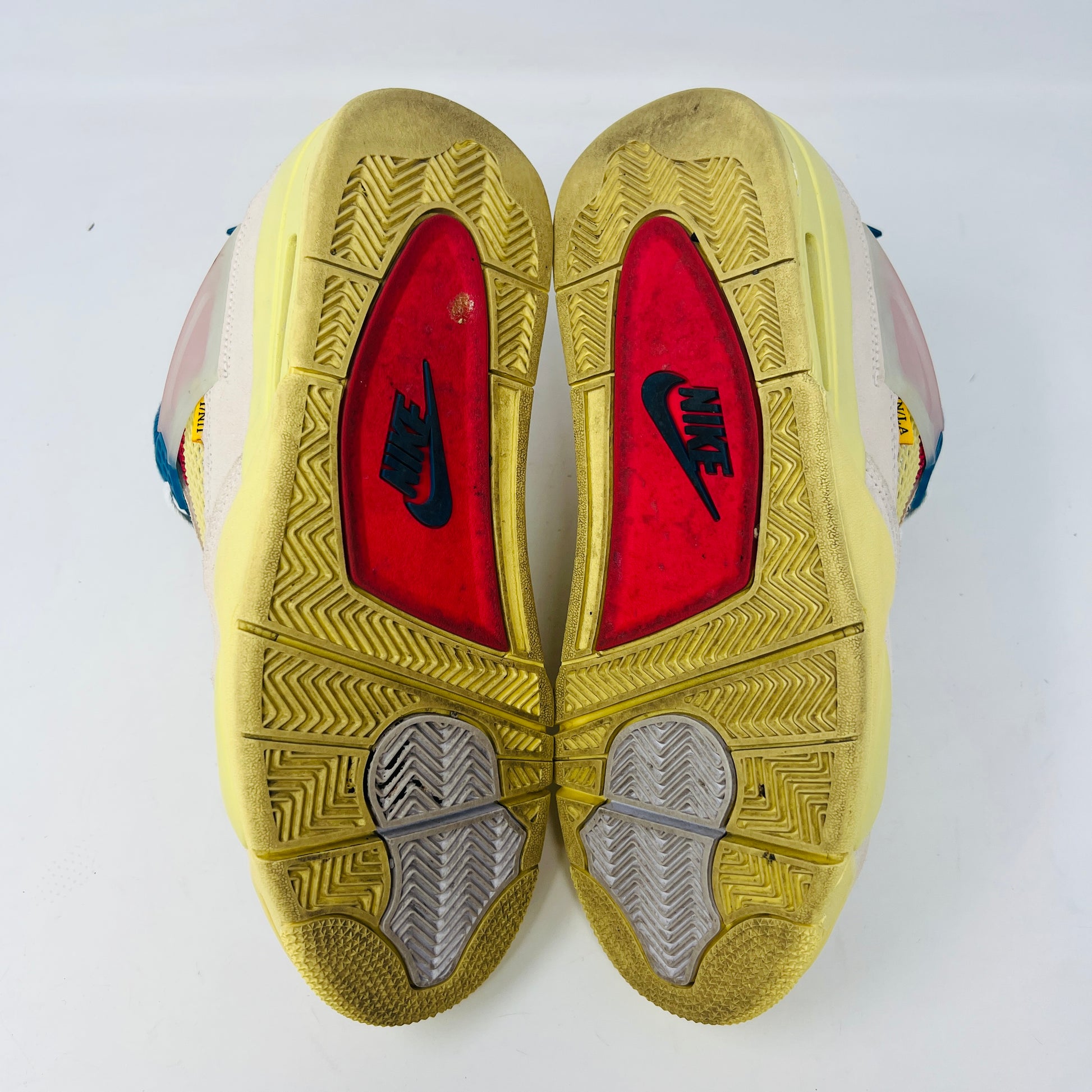 The Jordan 4 Retro Union Guava Ice sneaker from Jordan features a vibrant mix of beige, yellow, blue, and red on its clean uppers. It includes extra yellow laces packaged in a plastic bag alongside the shoe box.