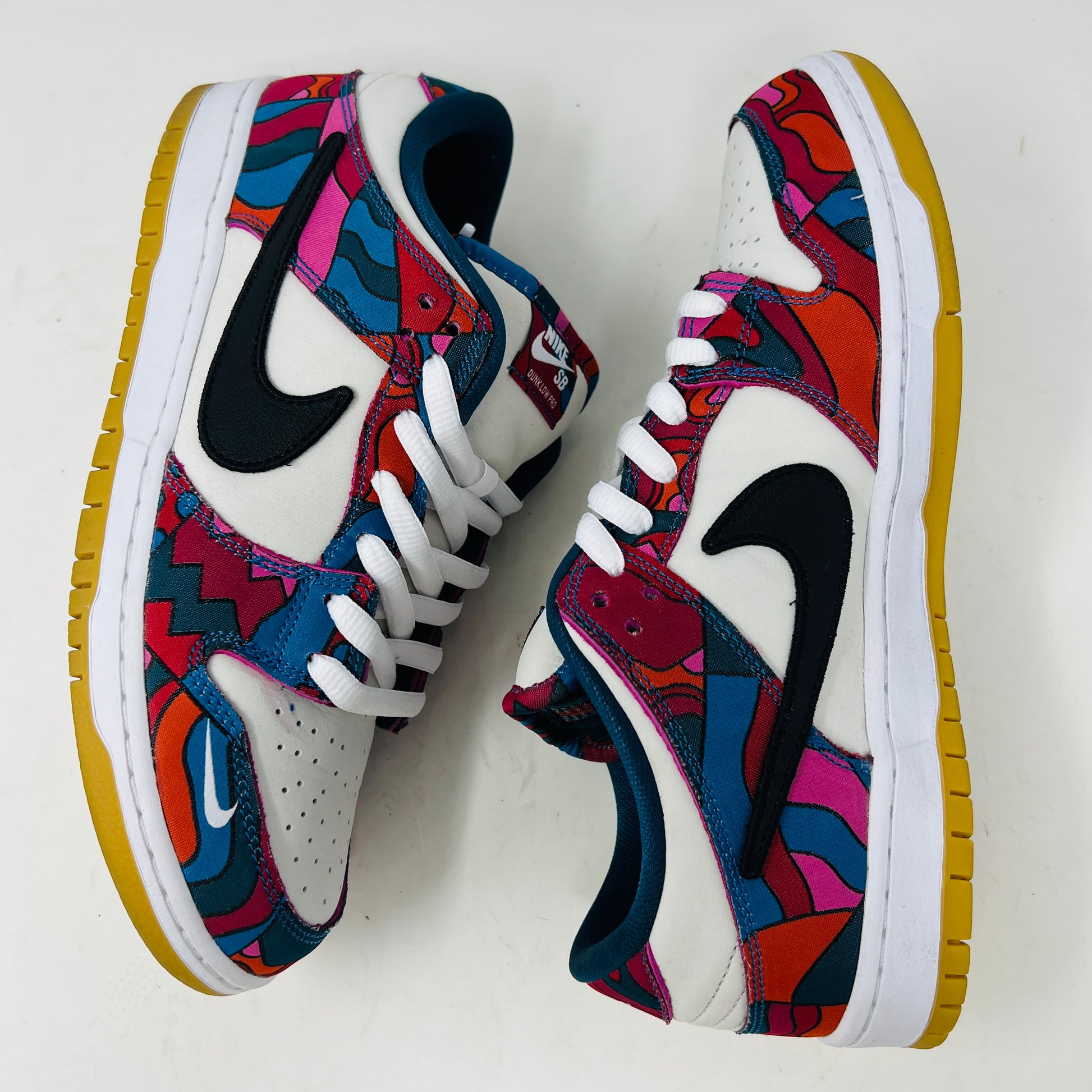 The Nike SB Dunk Low Pro Parra Abstract Art (2021) features a colorful design with abstract red, blue, and purple patterns on a white base. It includes clean uppers with a black swoosh, white laces, and comes in a green/yellow box with extra blue laces for added versatility.