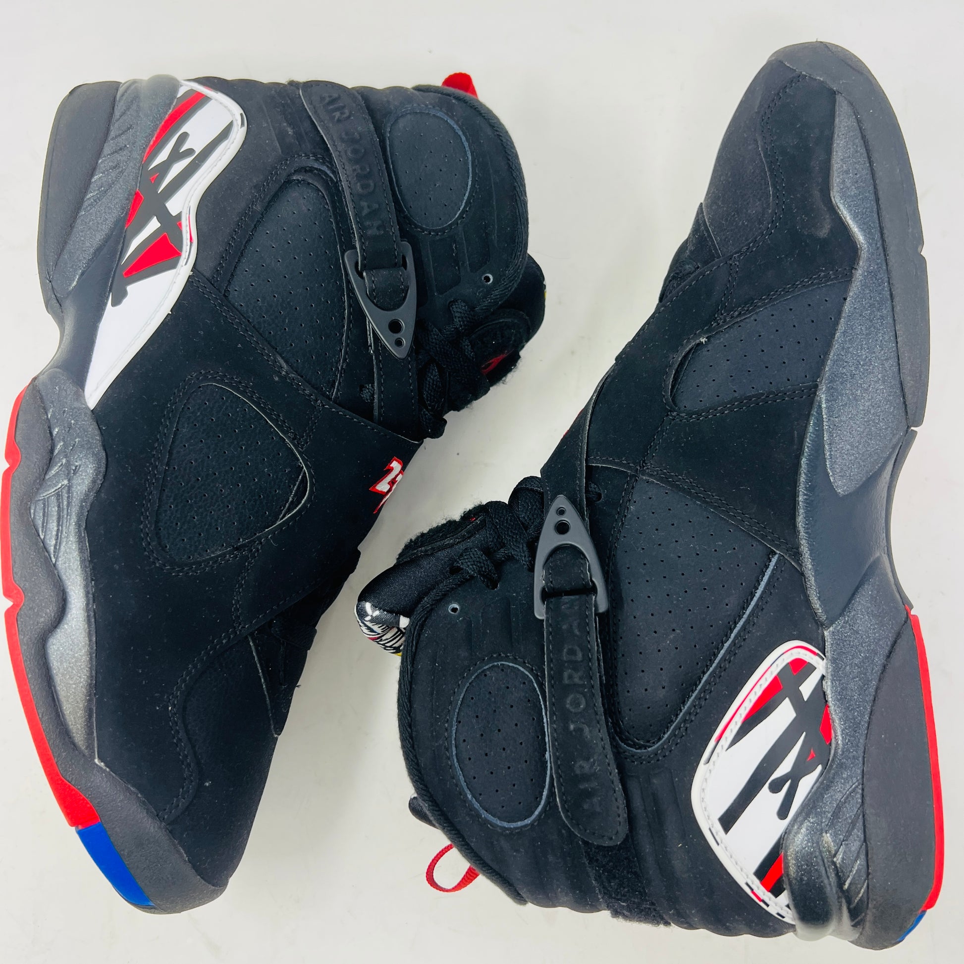 A Jordan 8 Retro Playoffs (2023) shoe, black and red with gray/red accents, features a high-top design with a strap, textured sole with blue hints, and clean uppers. Displayed on its Nike Air box in good condition, the label reveals size and Jordan brand details.