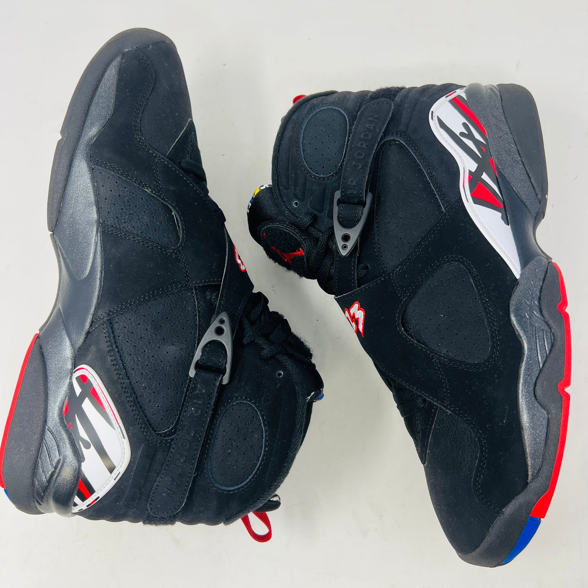 A Jordan 8 Retro Playoffs (2023) shoe, black and red with gray/red accents, features a high-top design with a strap, textured sole with blue hints, and clean uppers. Displayed on its Nike Air box in good condition, the label reveals size and Jordan brand details.