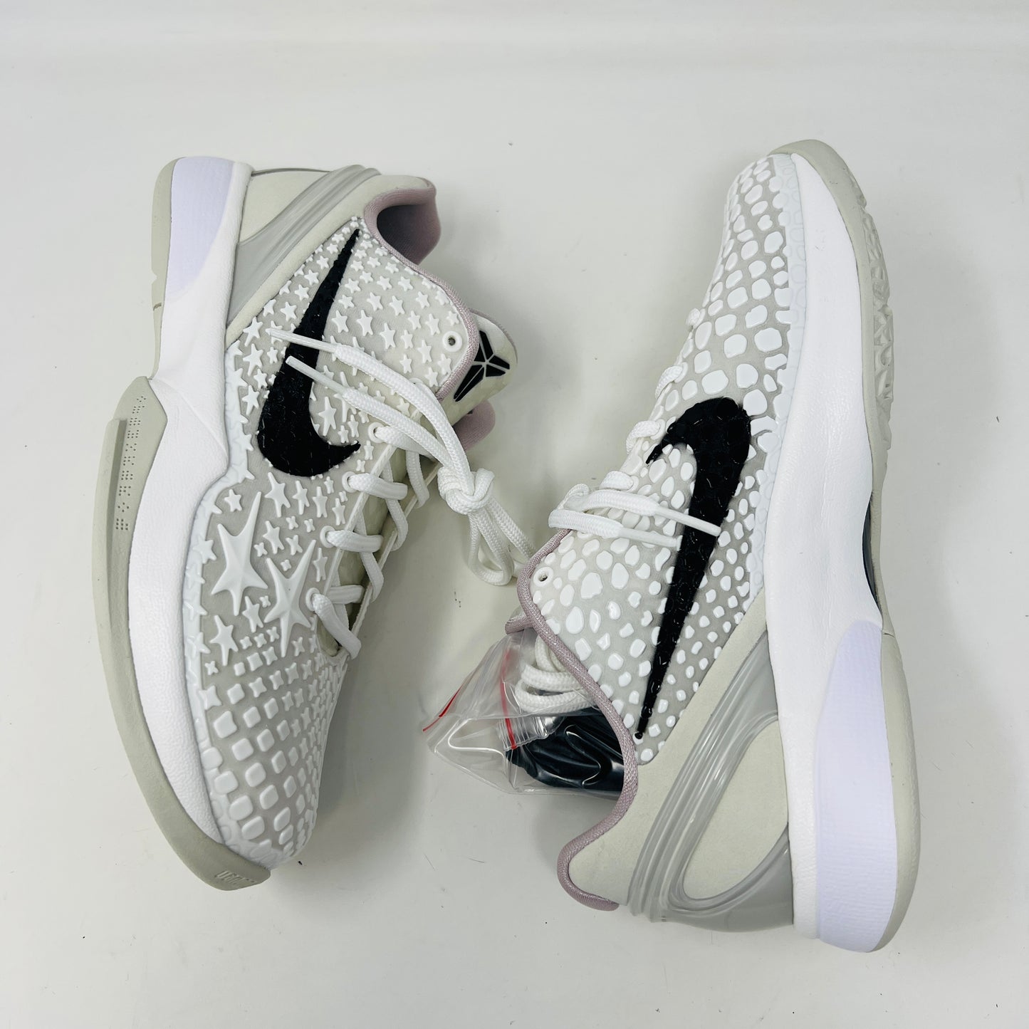 The fresh white Nike Kobe 6 Sail All-Star (GS) athletic shoe, showcasing a textured design and black swoosh logo, is presented on an orange box. Inside are plastic-wrapped accessories and extra laces for versatile style in 2024.