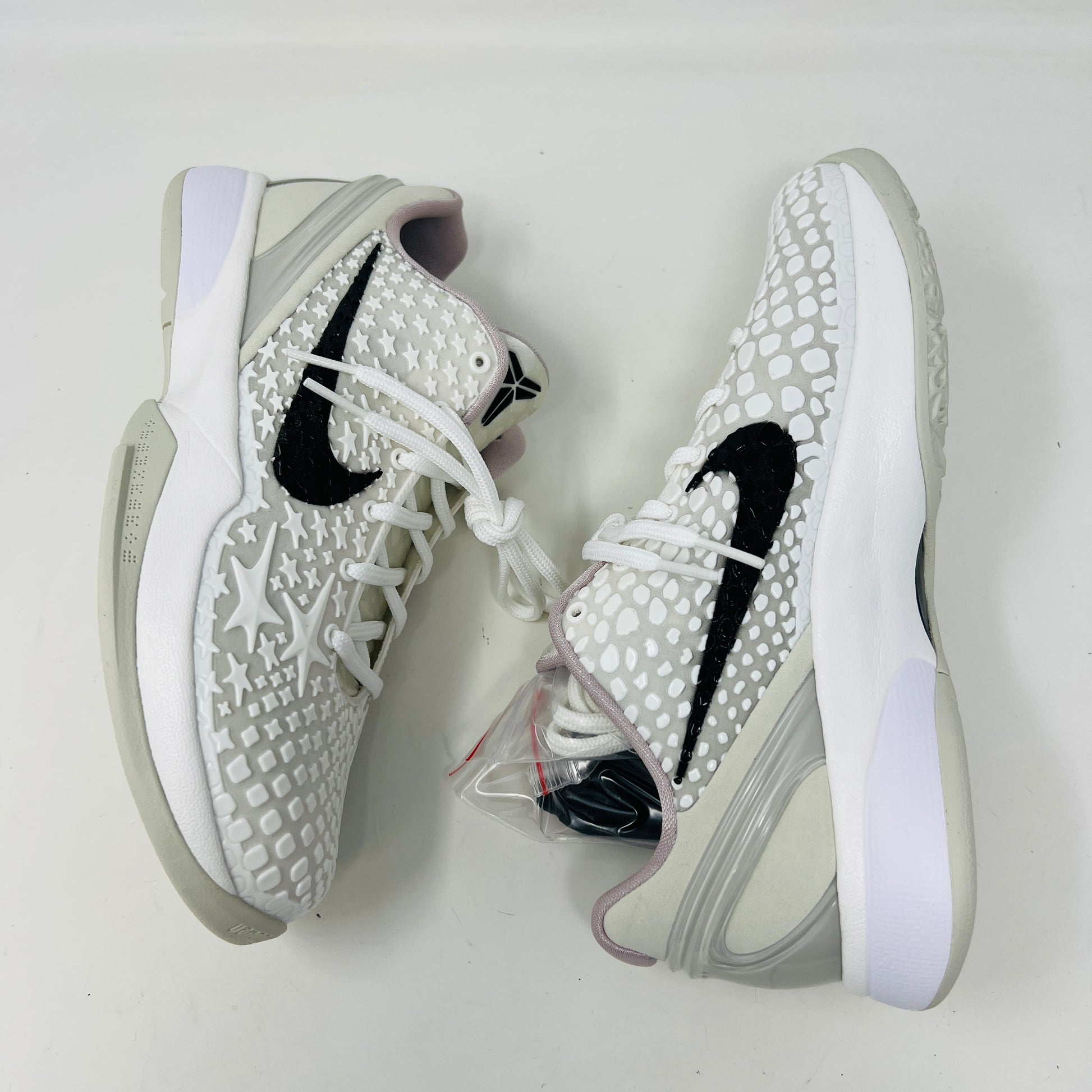 The fresh white Nike Kobe 6 Sail All-Star (GS) athletic shoe, showcasing a textured design and black swoosh logo, is presented on an orange box. Inside are plastic-wrapped accessories and extra laces for versatile style in 2024.