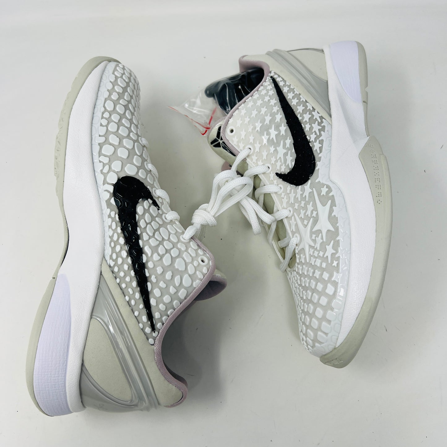 The fresh white Nike Kobe 6 Sail All-Star (GS) athletic shoe, showcasing a textured design and black swoosh logo, is presented on an orange box. Inside are plastic-wrapped accessories and extra laces for versatile style in 2024.