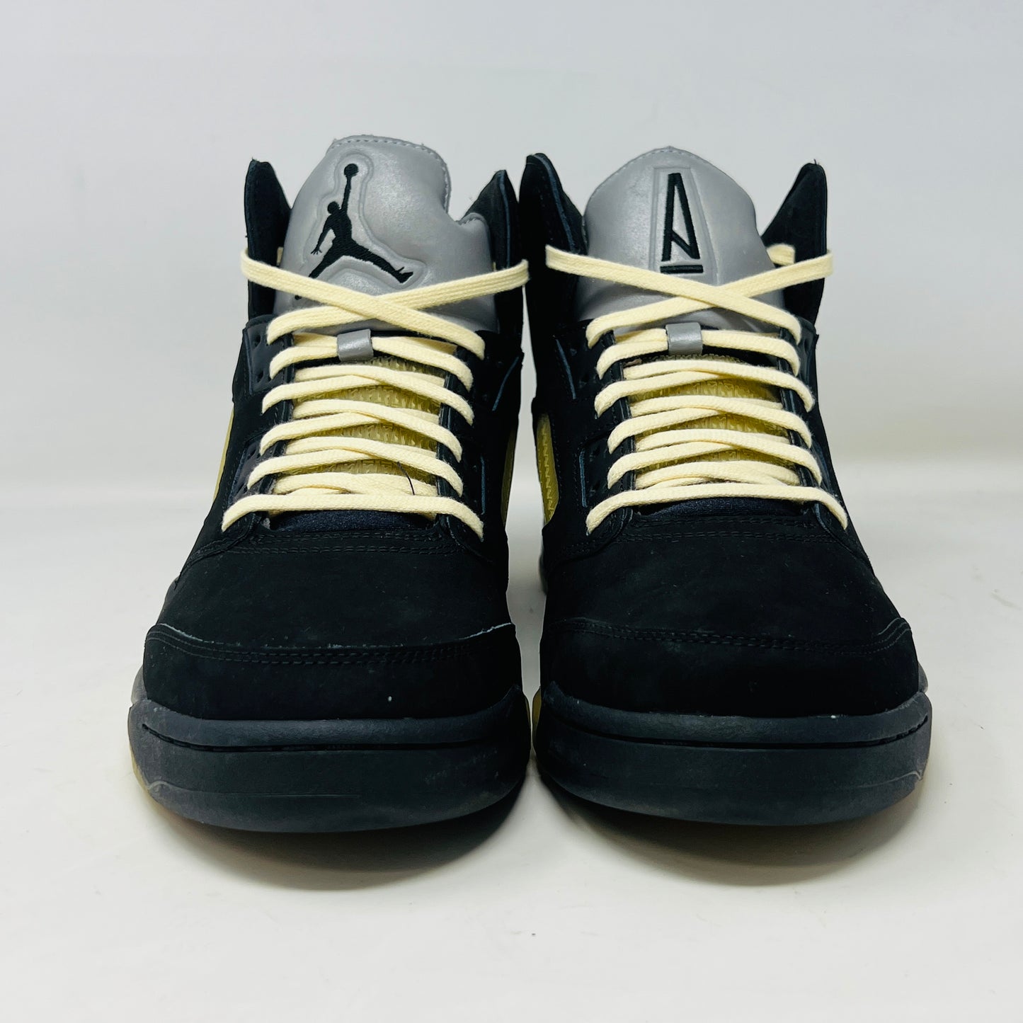 The Jordan 5 Retro A Ma Maniére Dusk sneaker, featuring sleek black and gold uppers and a translucent yellow sole, sits on a maroon shoebox. It includes black and white laces, extra pairs, and a yellow lace lock, all presented in front of the 2023 limited edition box from Jordan.