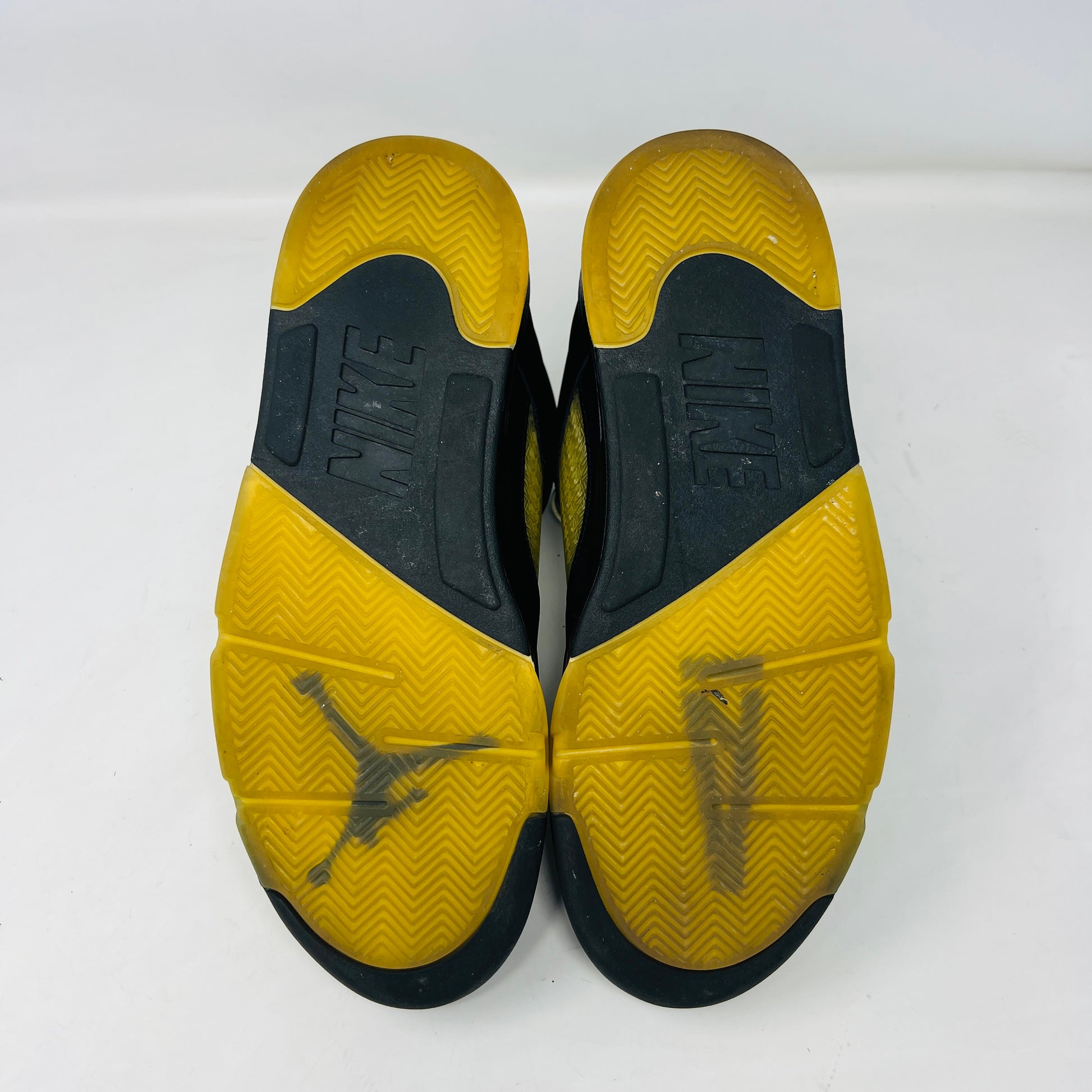 The Jordan 5 Retro A Ma Maniére Dusk sneaker, featuring sleek black and gold uppers and a translucent yellow sole, sits on a maroon shoebox. It includes black and white laces, extra pairs, and a yellow lace lock, all presented in front of the 2023 limited edition box from Jordan.