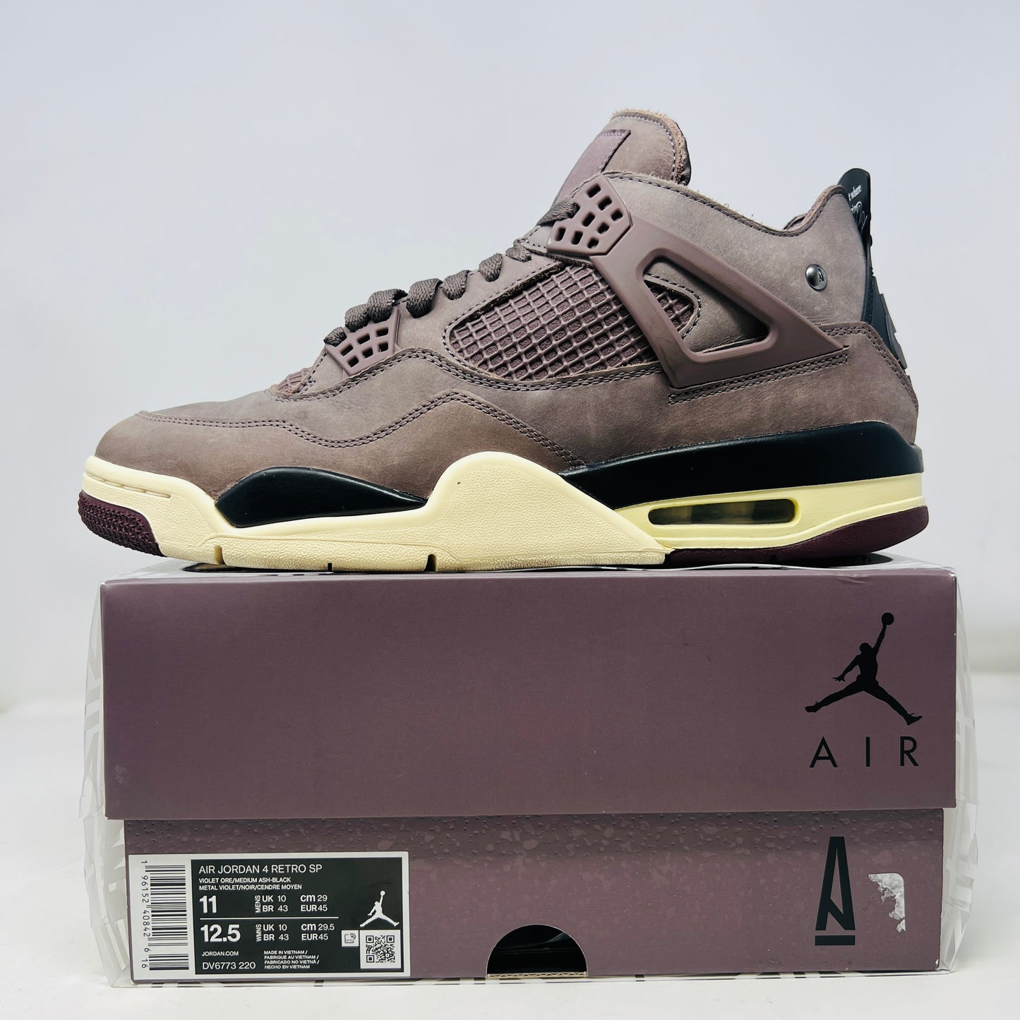 The Jordan 4 Retro SP A Ma Maniére Violet Ore sneakers sit elegantly on their matching box, featuring unique netting and black accents. The box displays size and brand details, emphasizing its immaculate condition.