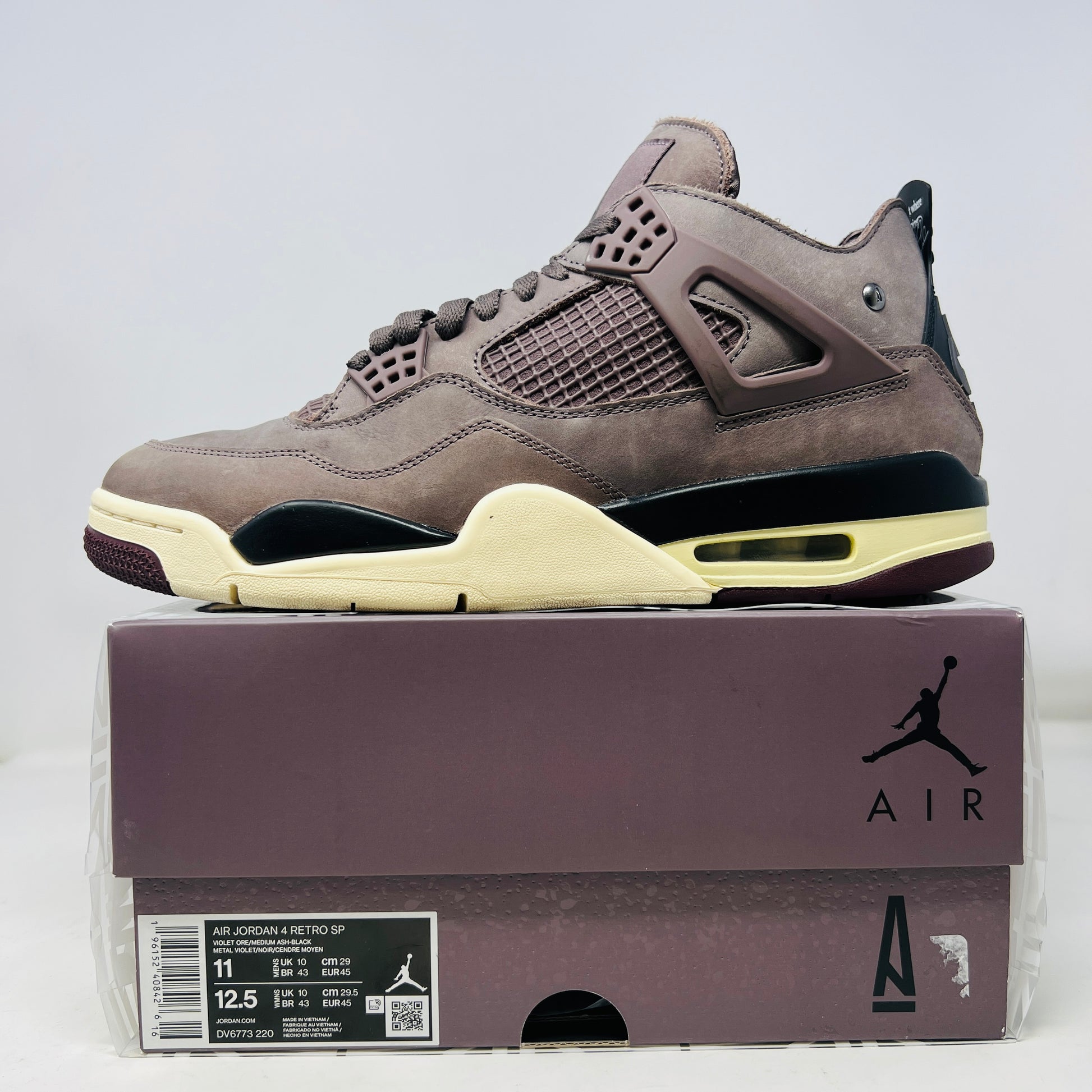 The Jordan 4 Retro SP A Ma Maniére Violet Ore sneakers sit elegantly on their matching box, featuring unique netting and black accents. The box displays size and brand details, emphasizing its immaculate condition.