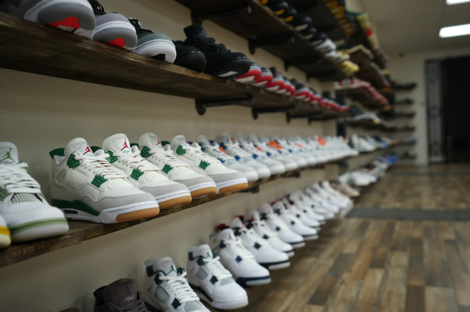 A shoe store with wooden shelves displaying neatly arranged sneakers. The focus is on a row of white sneakers with green accents, with more colorful sneakers progressively blurred into the distance. The floor is wooden, adding warmth to the scene.