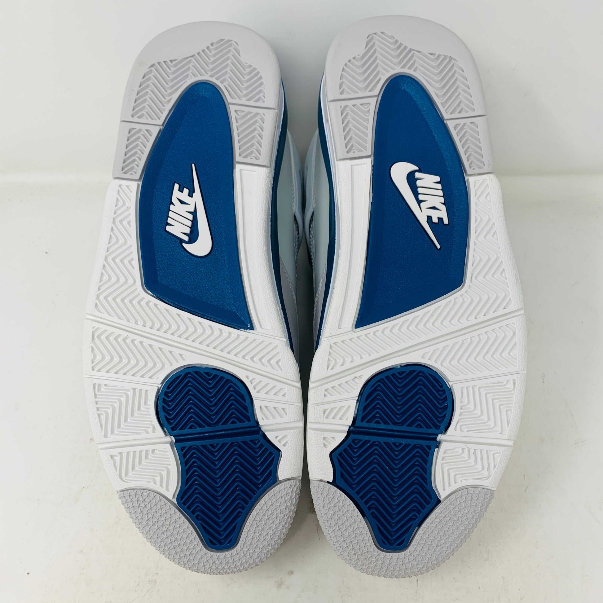 The Jordan 4 Retro Military Blue (2024) sneaker, with white and blue mesh details and a visible air cushion, rests on a black speckled NIKE AIR box with bold orange text. It is 100% authentic, including orange tags, ensuring it’s brand new.