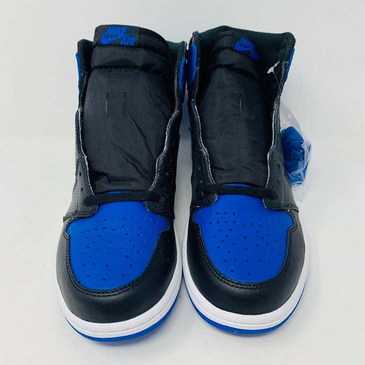 A pair of brand new black and blue Jordan 1 Royal 2017 high-tops are showcased on a black and red Nike box, with a small plastic bag holding authentic blue laces attached to one shoe.